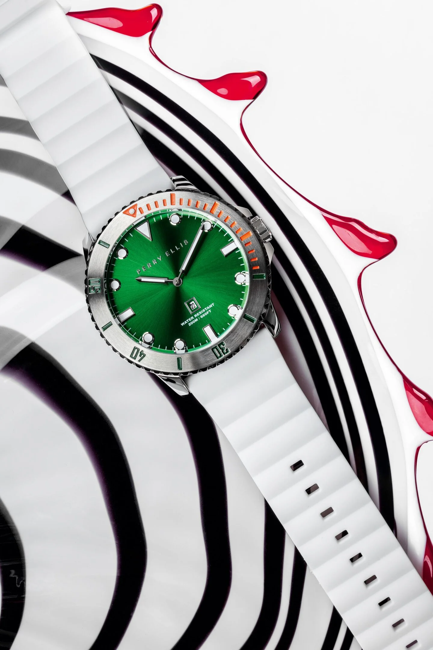 A green wristwatch with a stainless steel bezel and orange and green accents, placed on a white surface with a Sony PlayStation controller with black and white buttons and a red liquid splash design.