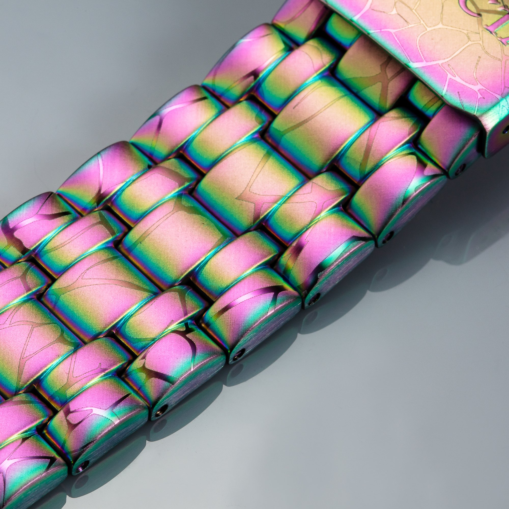 Close-up of a metallic rainbow-colored chain or bracelet with interconnected square links, placed on a plain white surface.