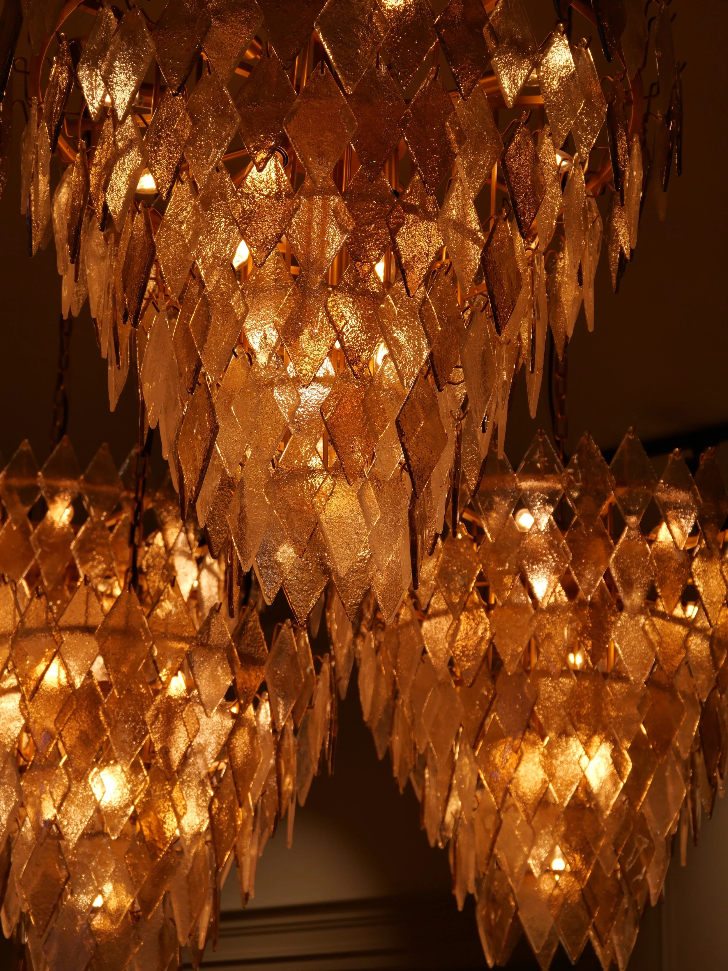 Un lustre en cristal doré suspendu, illuminé et décoratif, avec des morceaux en forme de diamants.