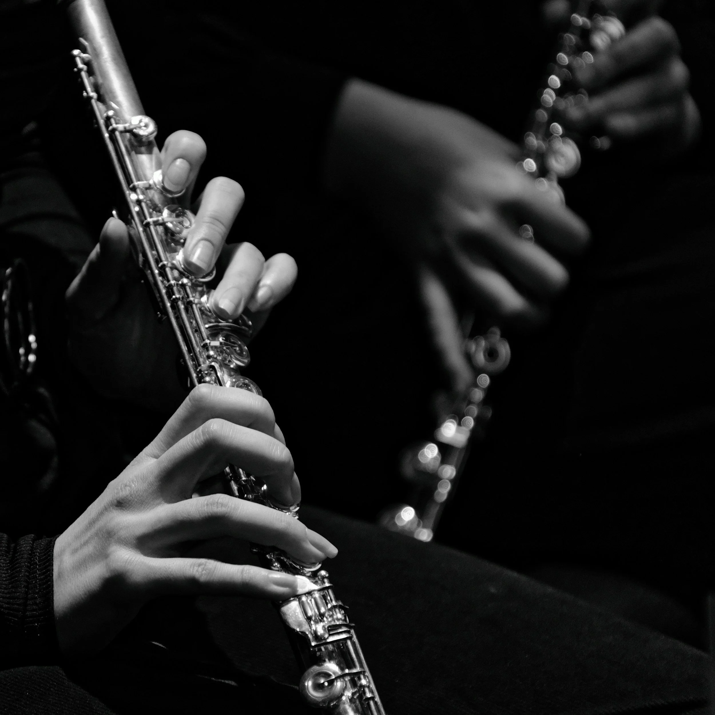 Close-up of a person's hands playing a flute, focusing on the fingers and instrument against a dark background.