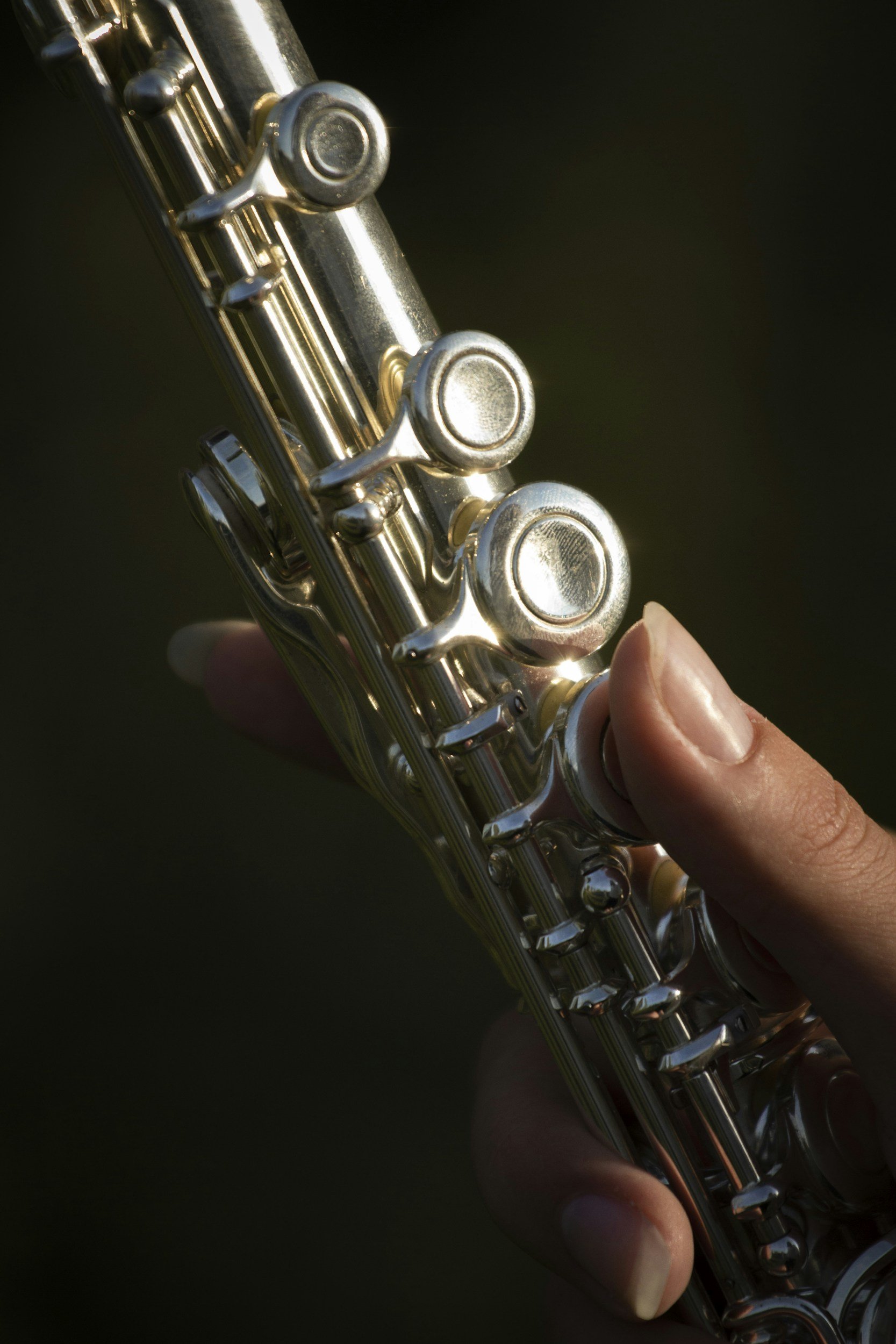 Close-up of a person holding a silver flute, with fingers on the keys, against a dark background.
