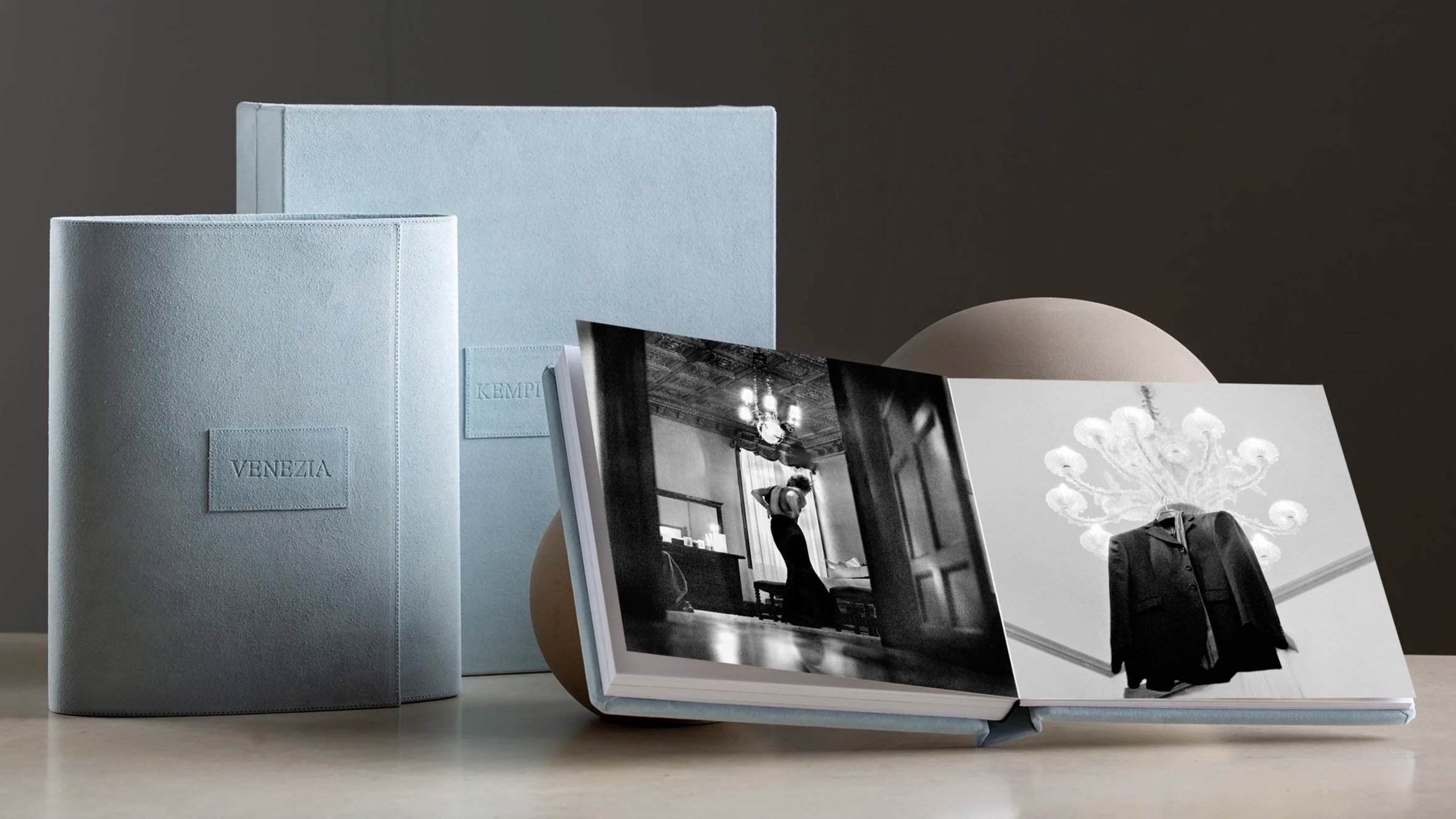 A collection of photo albums and books on a table, with some standing upright and others lying flat, including a large light blue album labeled 'VENEZIA' and two black-and-white photography books.