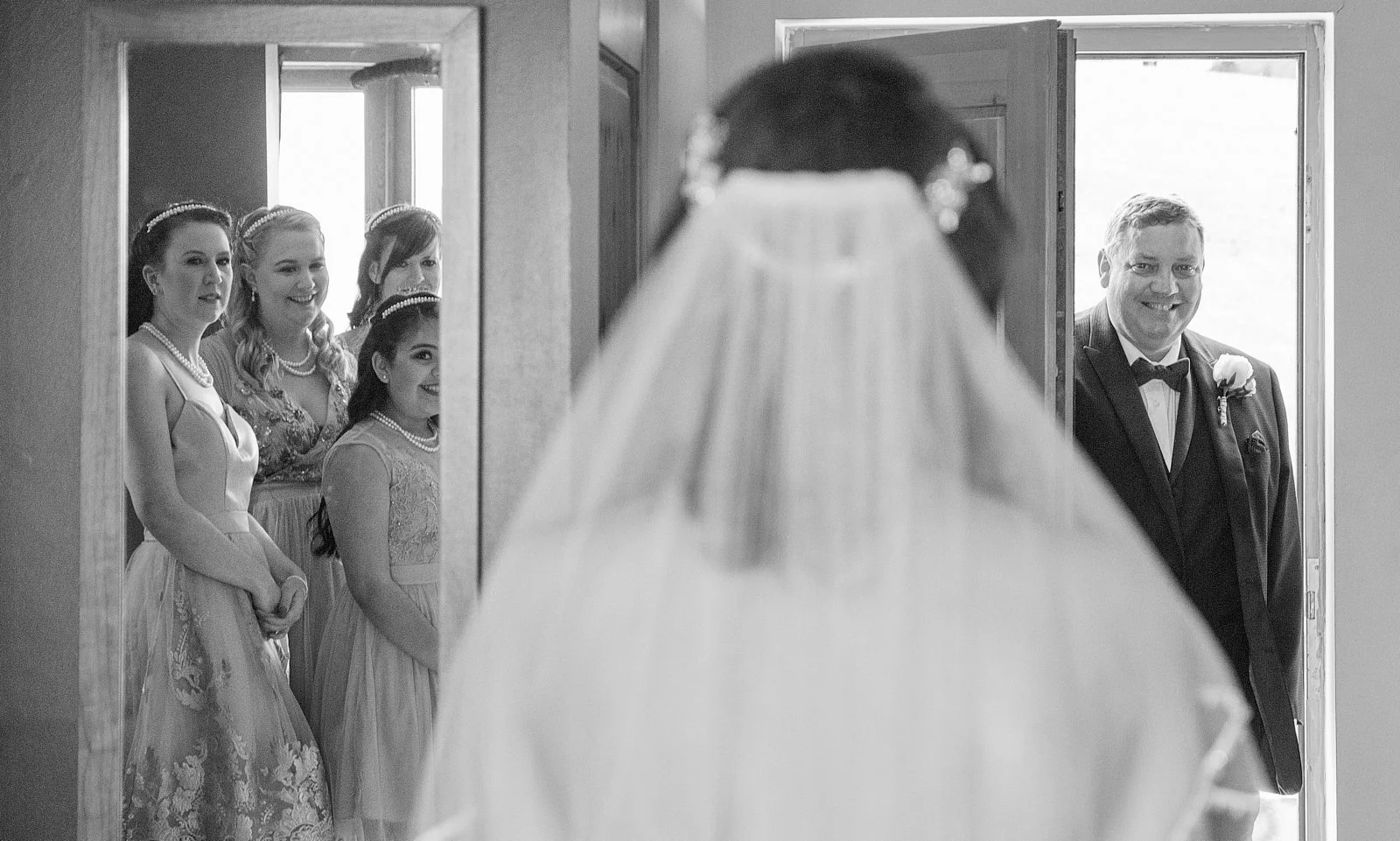 Bride and groom looking at each other as the bride's friends and bridesmaids watch from behind a mirror.