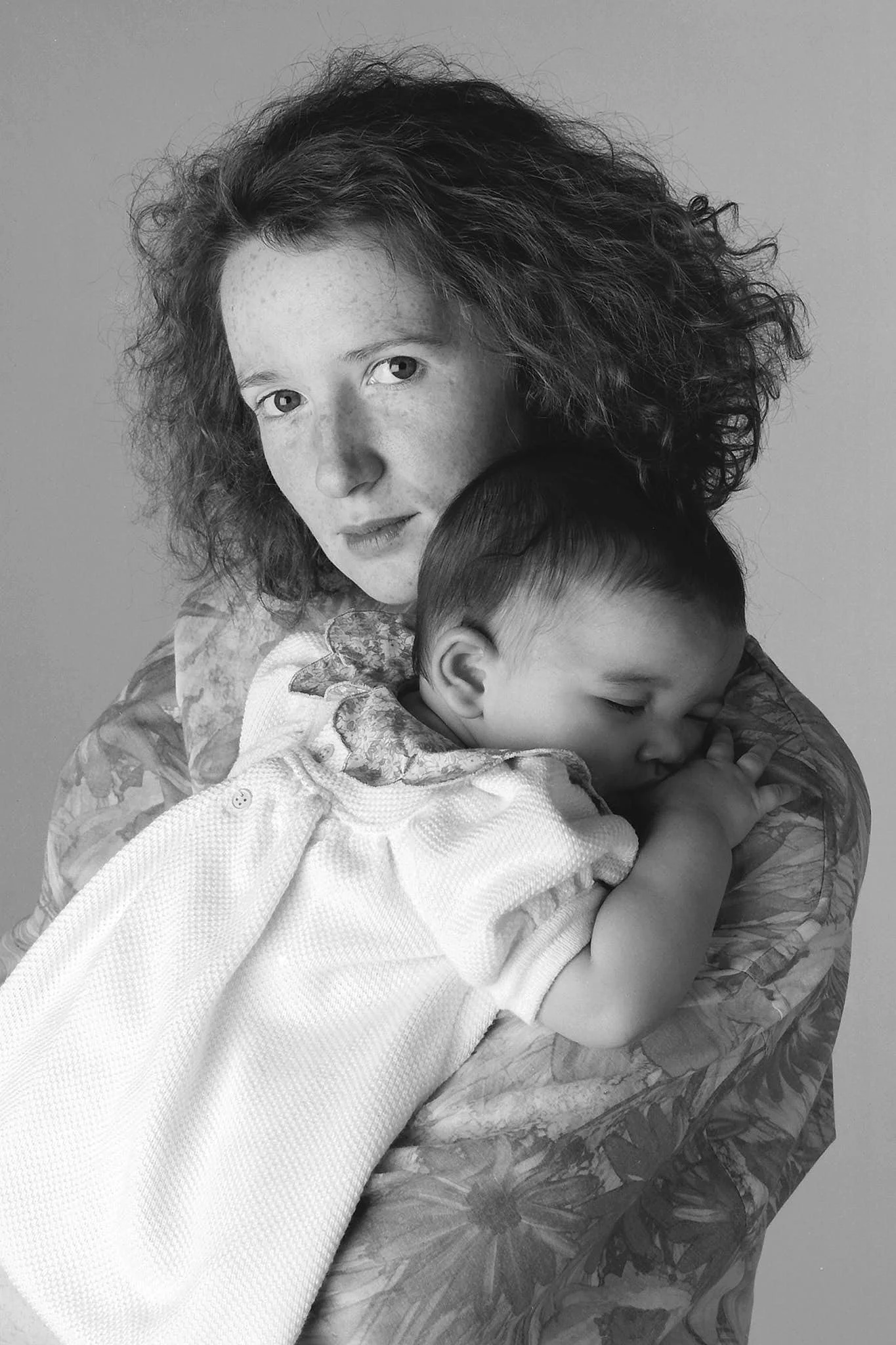 A woman with curly hair holding a young child, with her head close to the child's head, both appearing calm and affectionate.