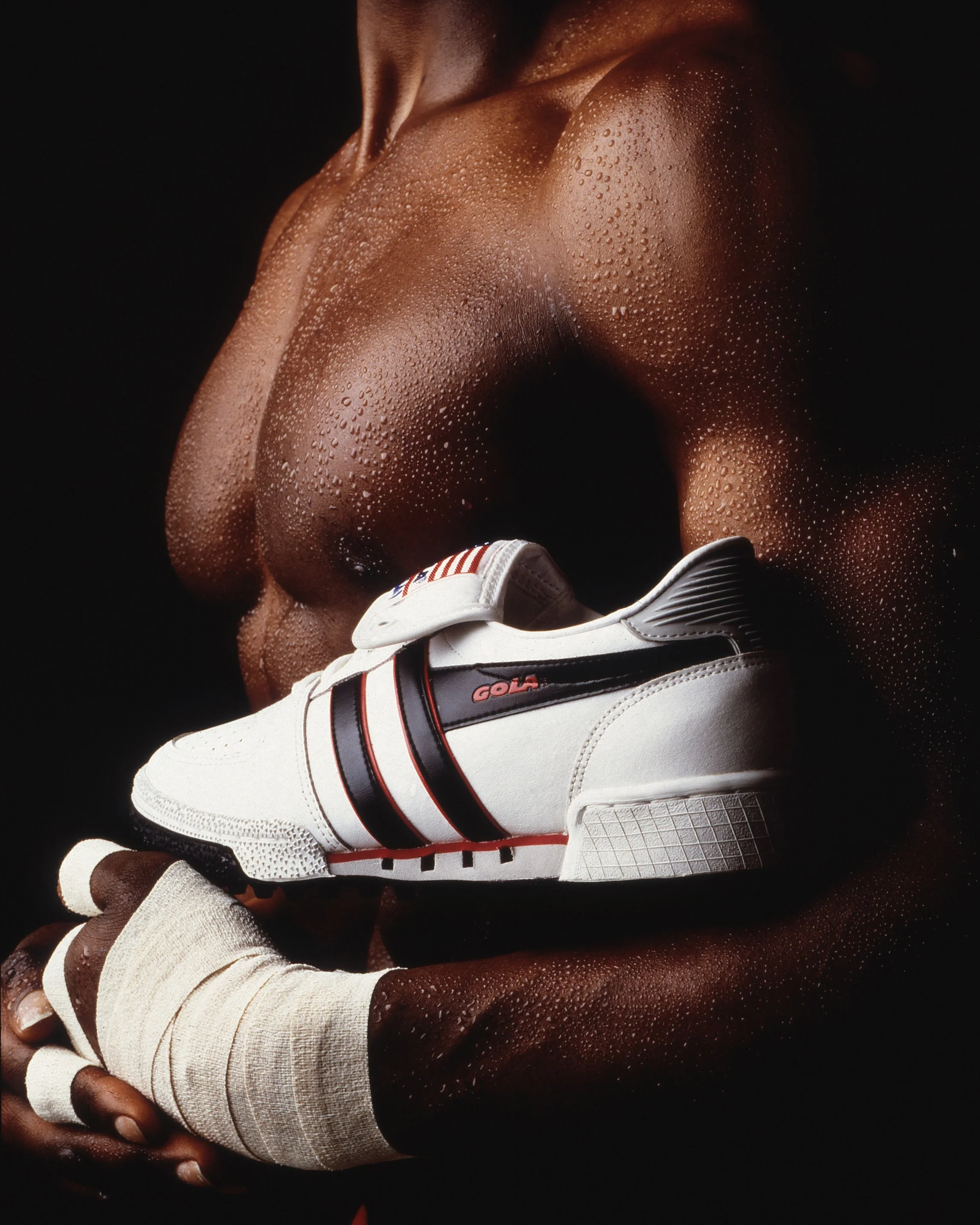 Close-up of an athlete's hand wearing a white sports glove, gripping a football, with a focus on the gloved hand and the textured surface of the football against a black background.