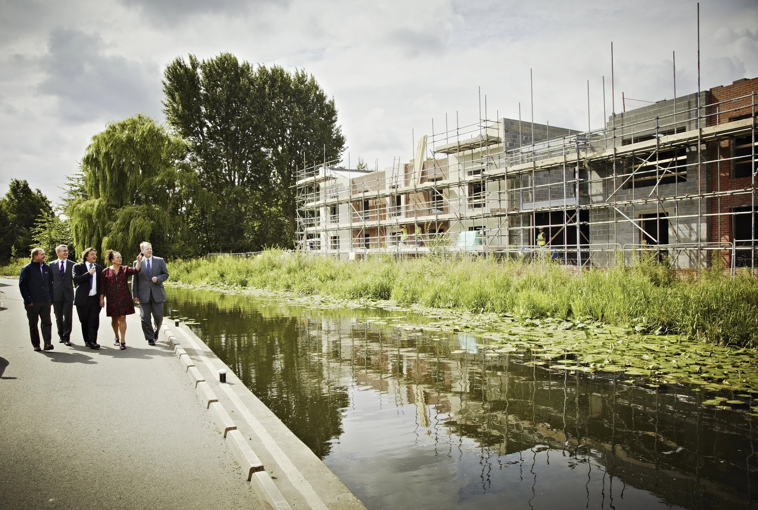 Group of five leaders walking along a canal with construction site in background.