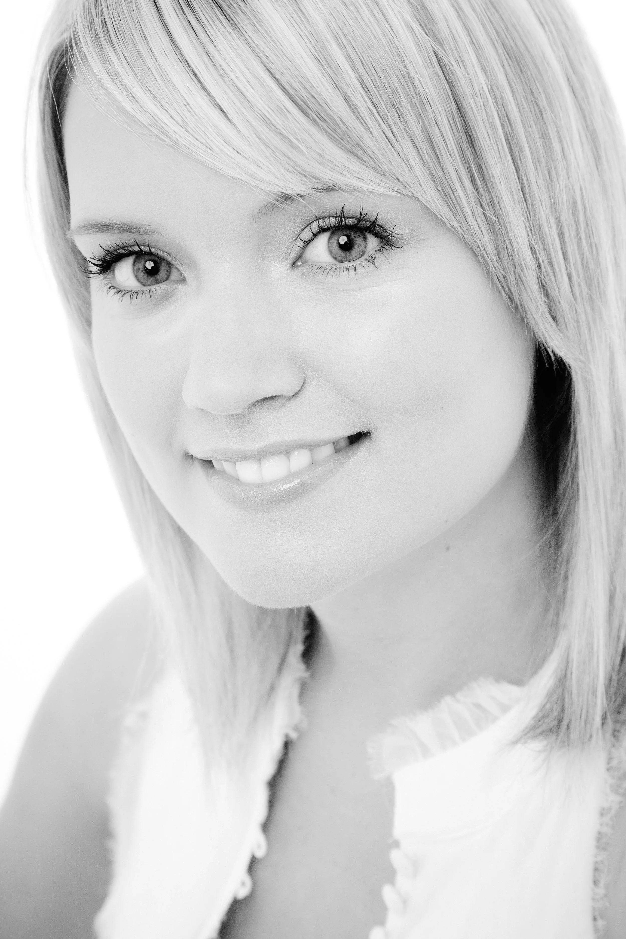 Close-up of a smiling woman with blonde hair and light-colored eyes, wearing a white top, in black and white.