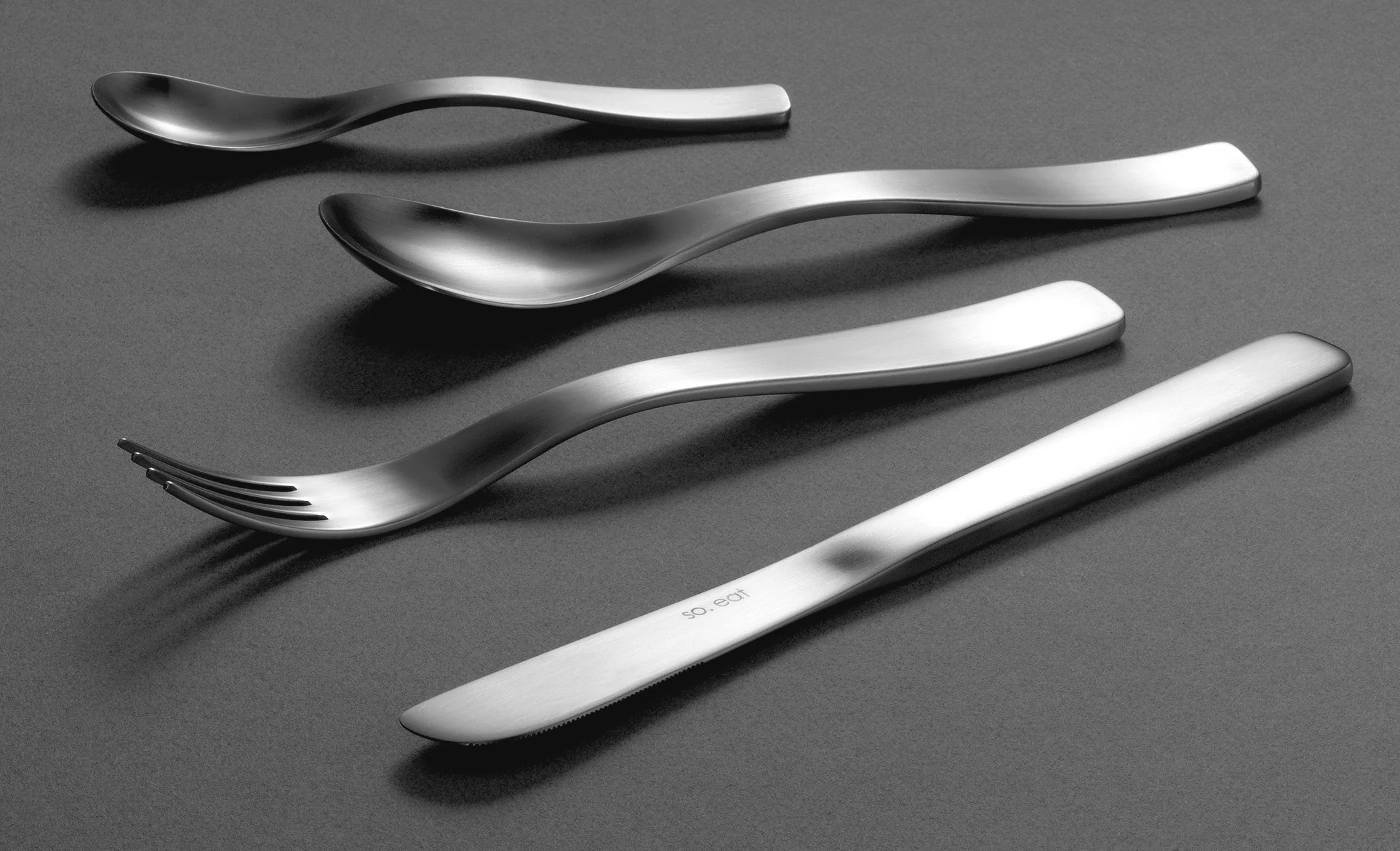 A set of metallic cutlery including spoons and a fork arranged on a dark surface.