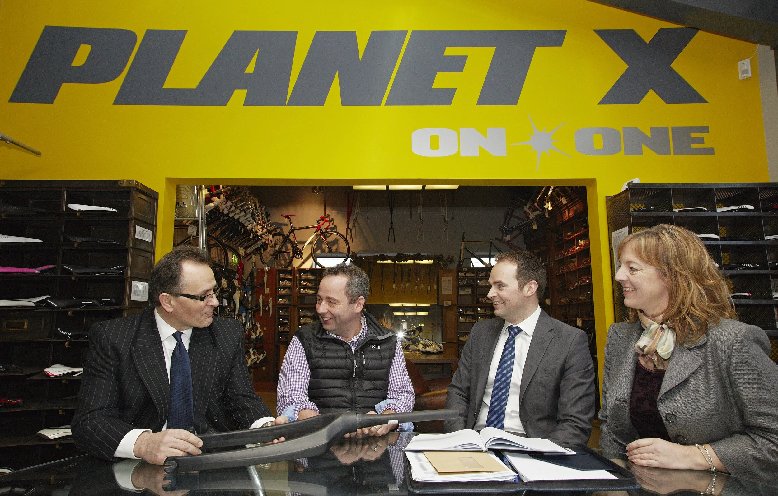 Group of four people conversation inside a bicycle shop with shoes and bicycles in the background.
