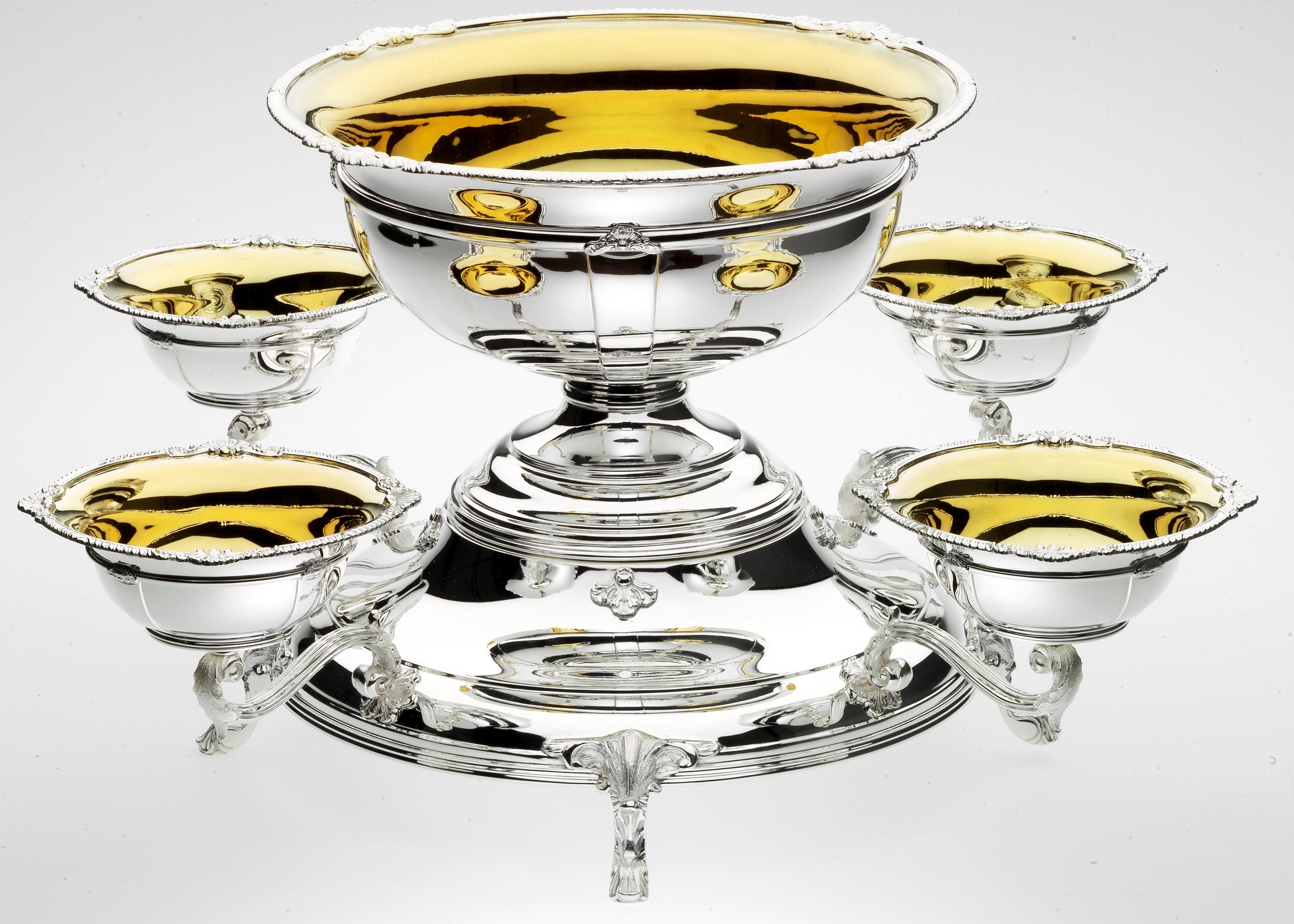 Silver and gold decorative bowls with ornate designs, reflecting a white background.