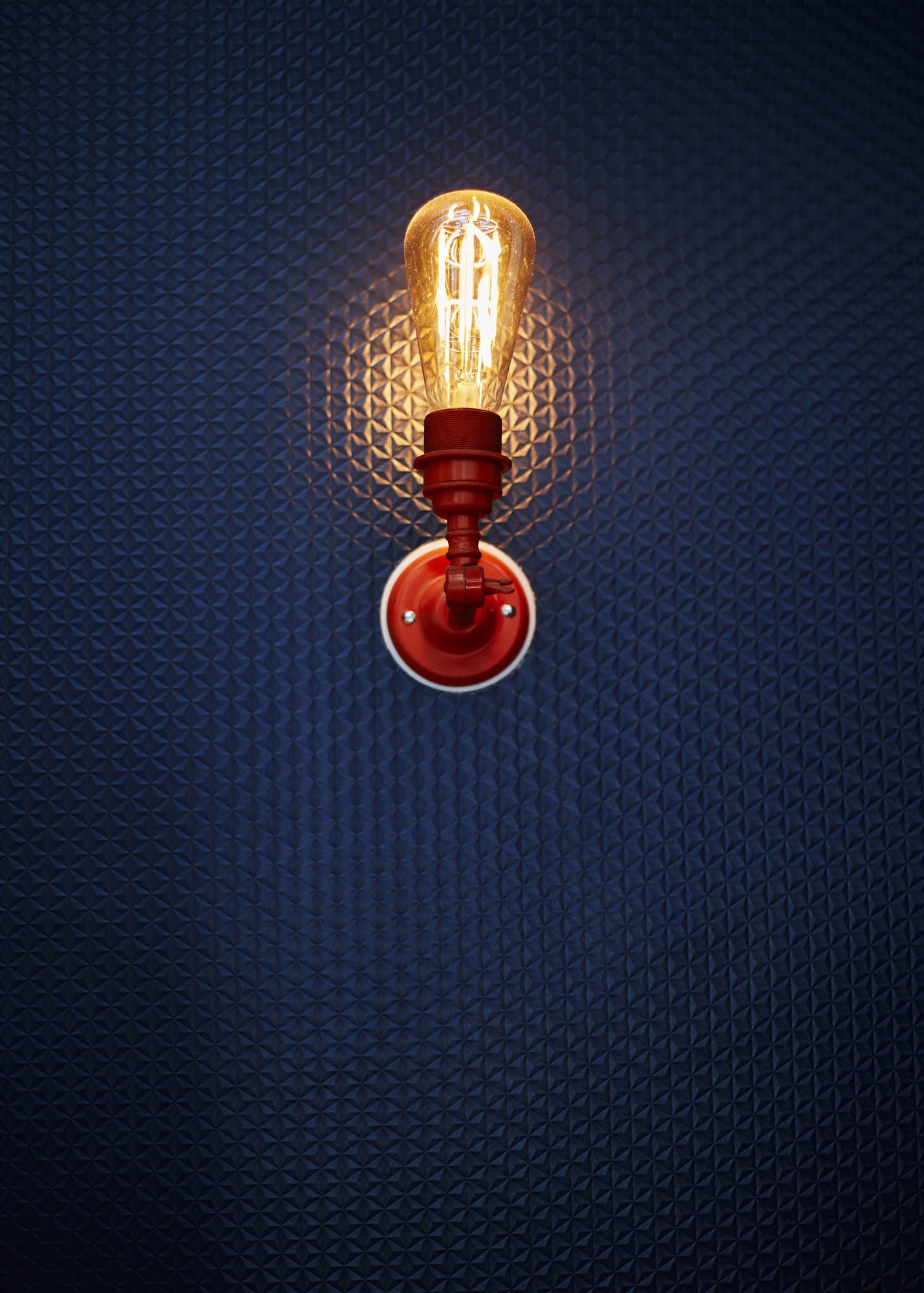 Close-up of an illuminated vintage Edison-style light bulb mounted on a wall with a textured black surface.