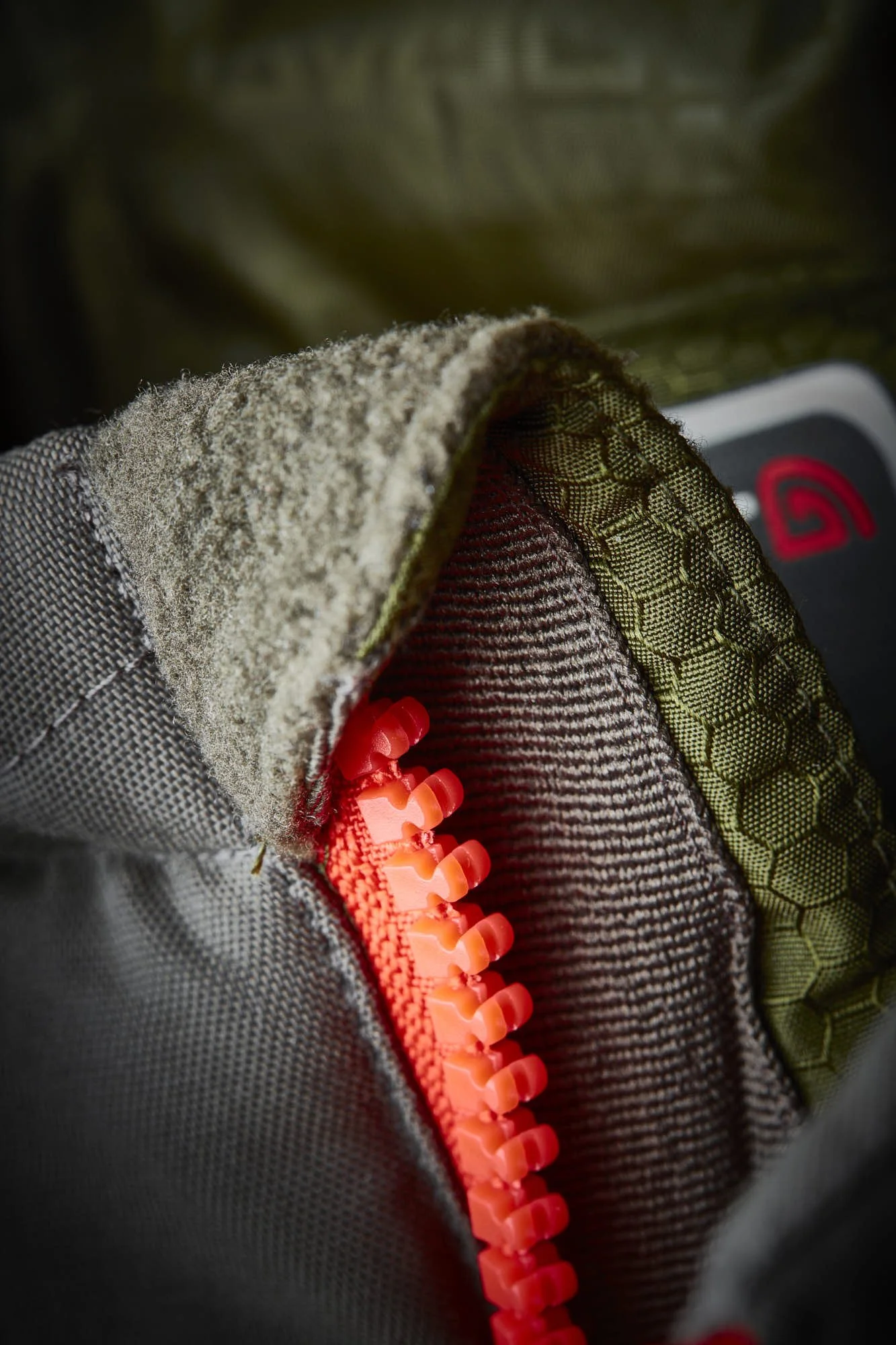 Close-up of a grey, textured fabric and a bright orange zipper on a sneaker, with another shoe visible in the background.