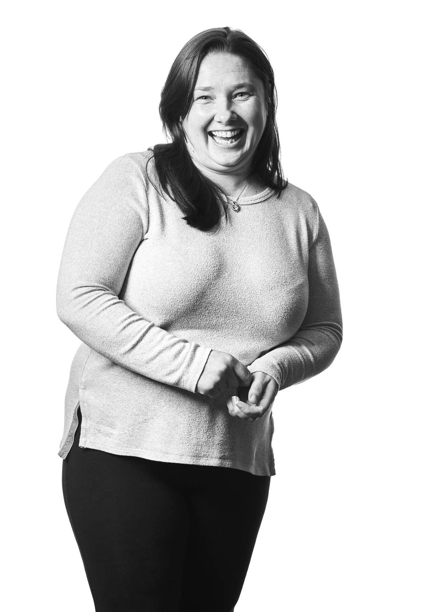 Black-and-white photo of a smiling woman with shoulder-length dark hair, wearing a long-sleeved top and standing against a plain background.