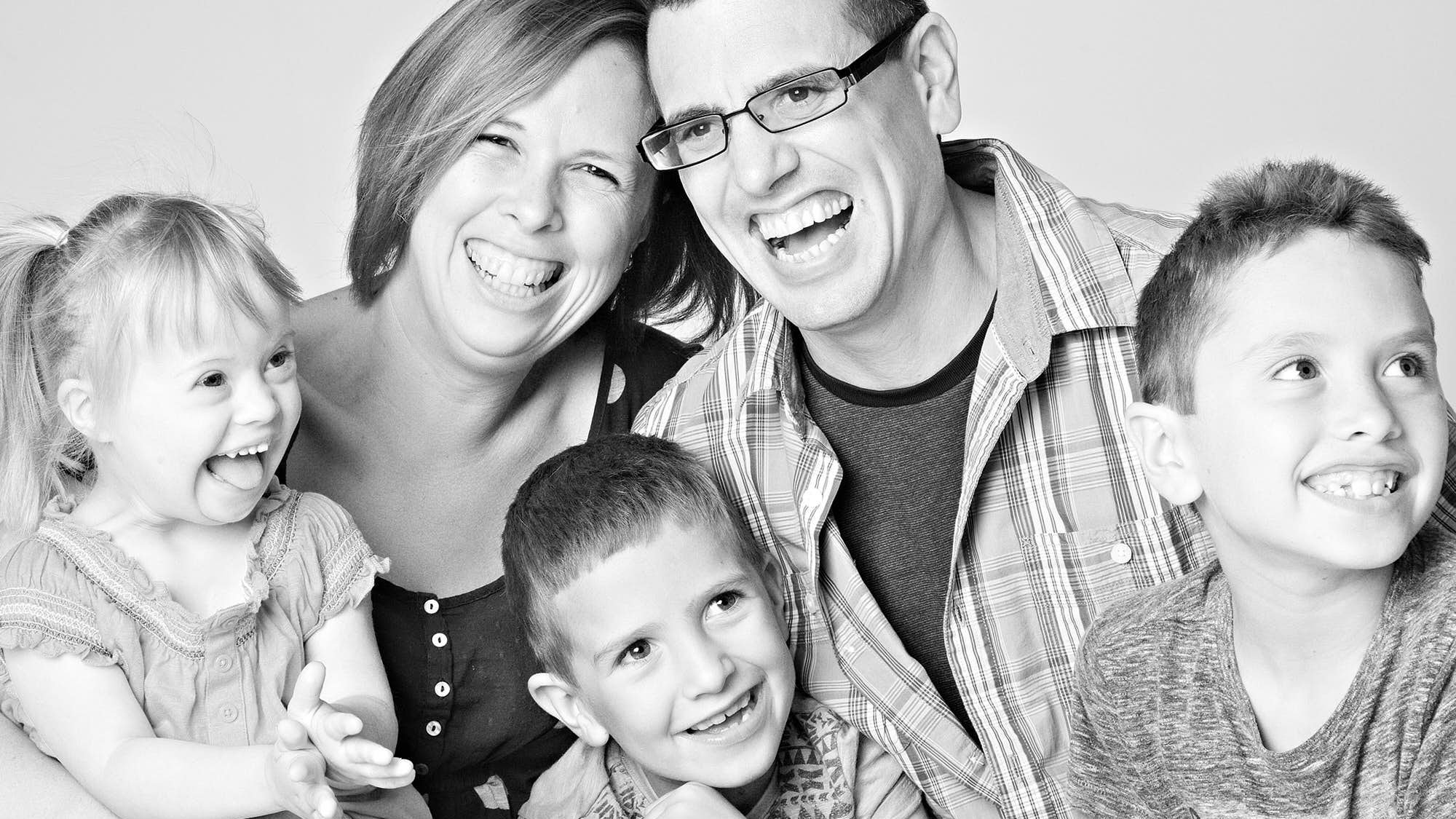 Black and white photo of a smiling family of six, including two women, one man, and three children, all appearing happy and joyfully posing together.
