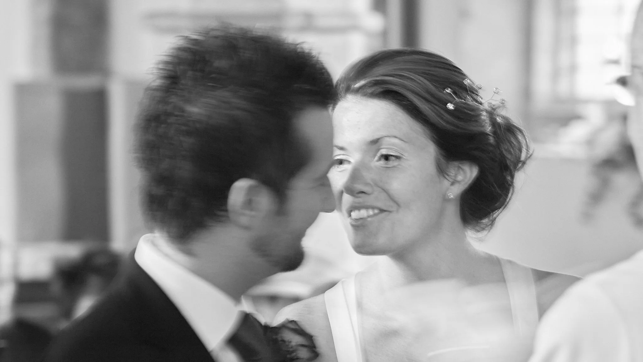 A black and white photo of a man and woman facing each other, smiling and about to kiss, in an indoor setting.
