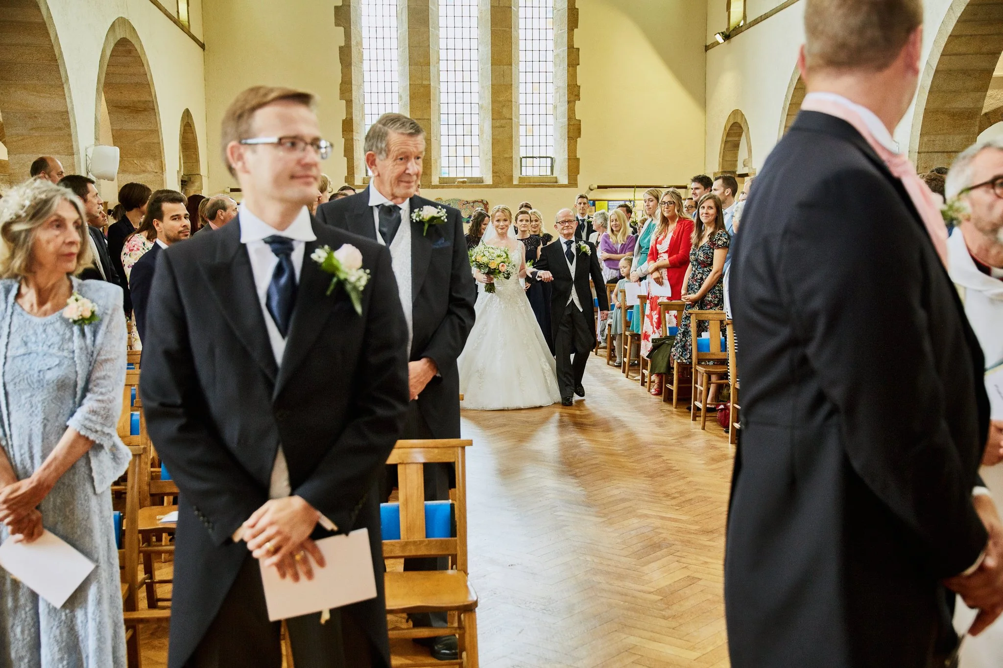 A wedding ceremony inside a church with guests seated and the bride and groom walking down the aisle.