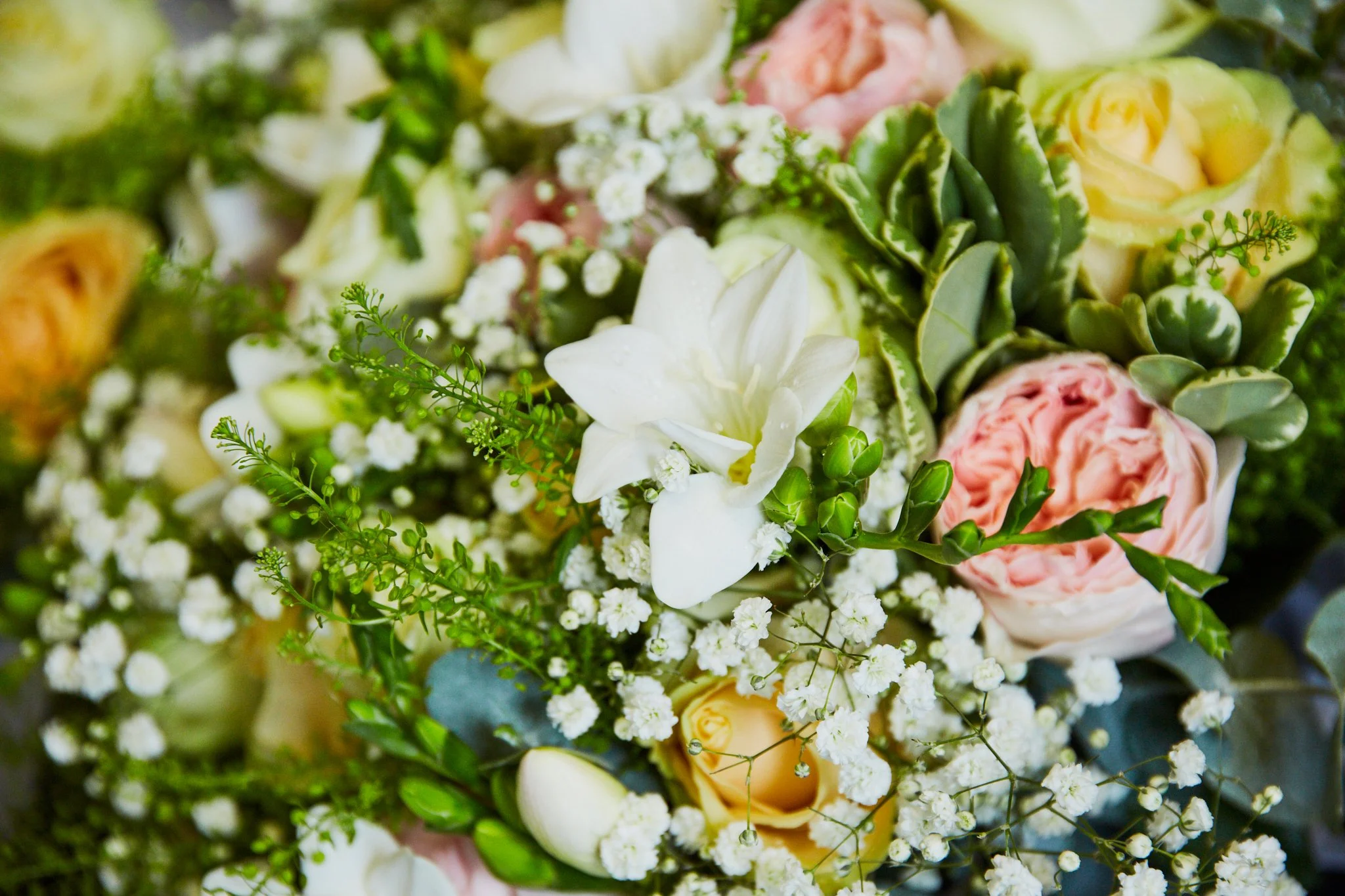 A close-up of a bouquet of flowers that includes white lilies, pink roses, small white flowers, and green foliage.