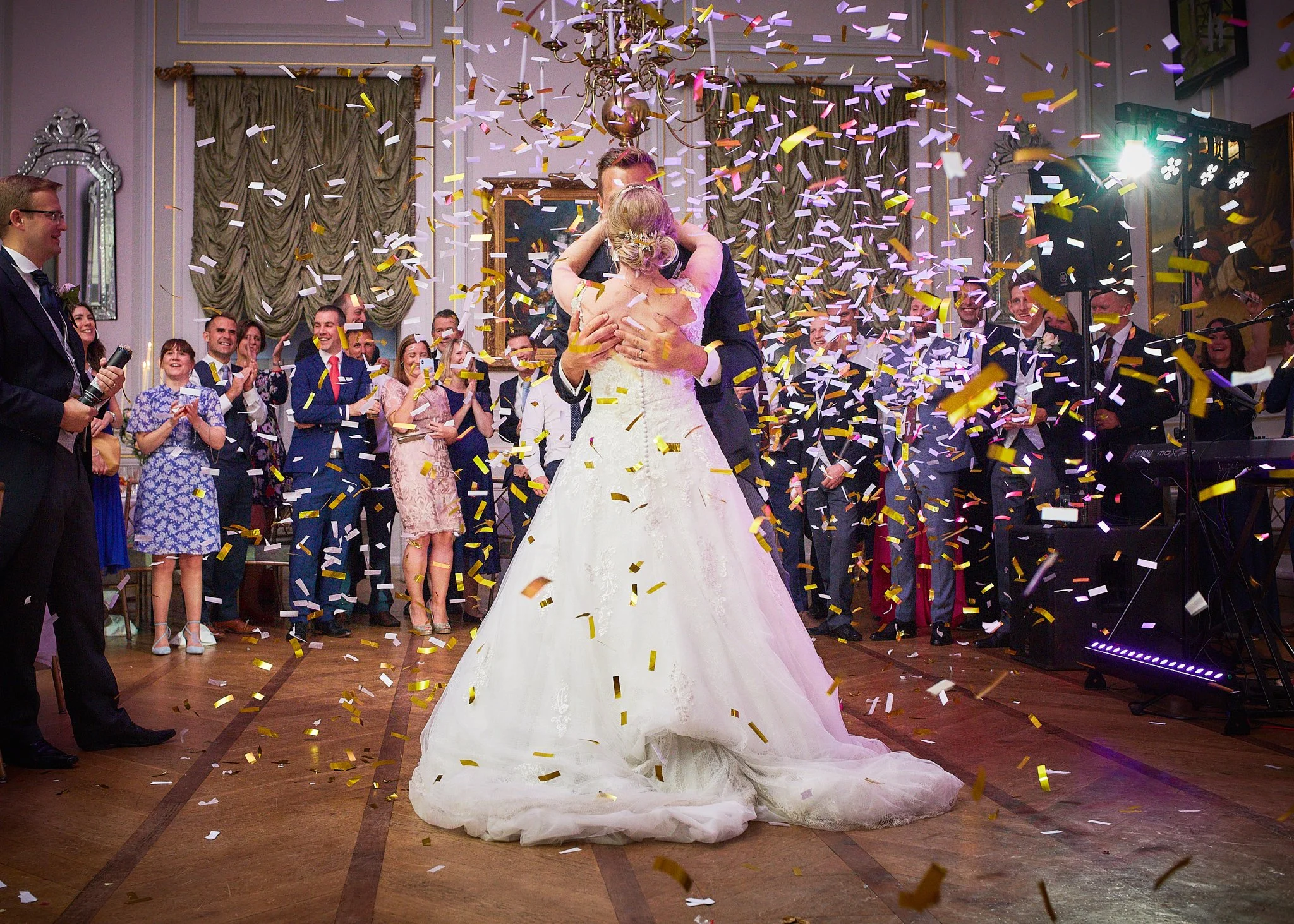 Couple dancing at a wedding reception with confetti falling around them, surrounded by guests smiling and clapping.