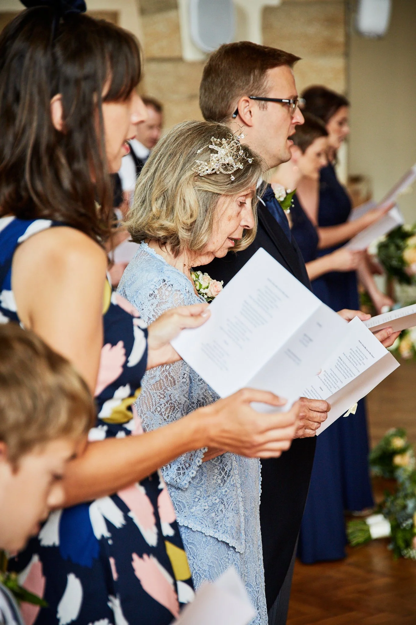 People participating in a wedding or religious ceremony, holding programs or booklets and standing side by side.