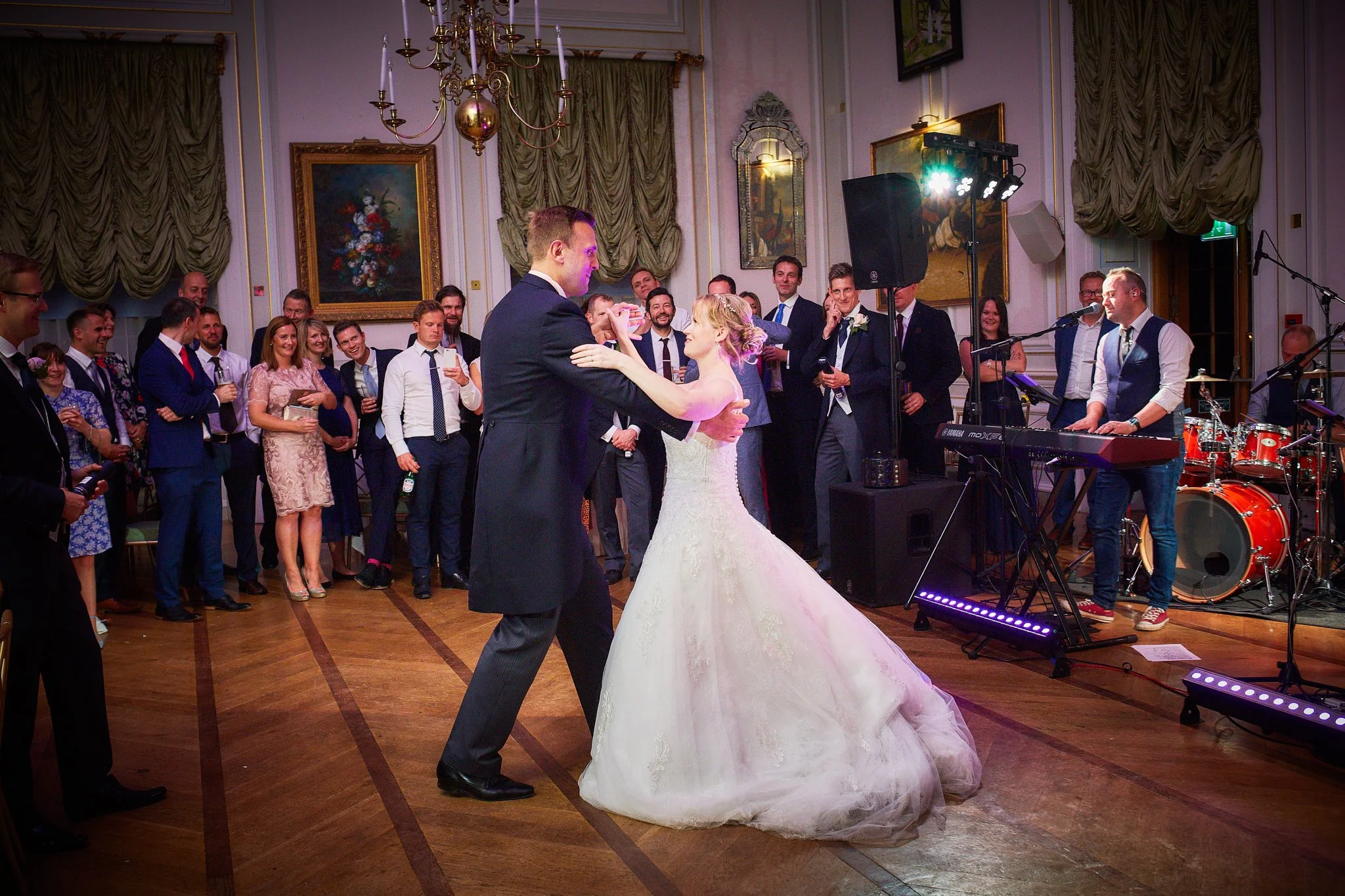 A bride and groom dancing at a wedding reception with guests watching and smiling in a decorated banquet hall.