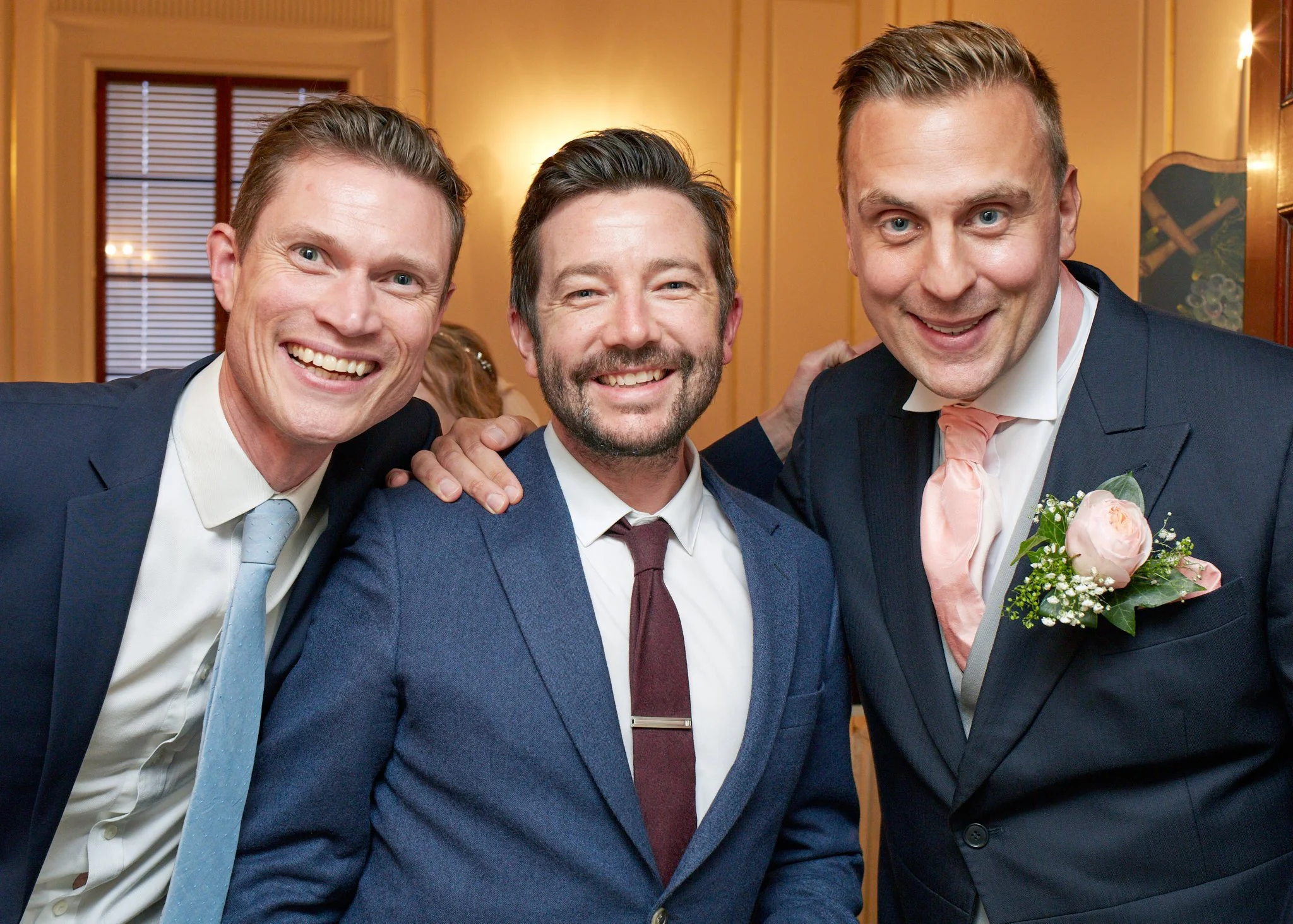 Three men dressed in suits, smiling, at a formal event in a warmly lit room.