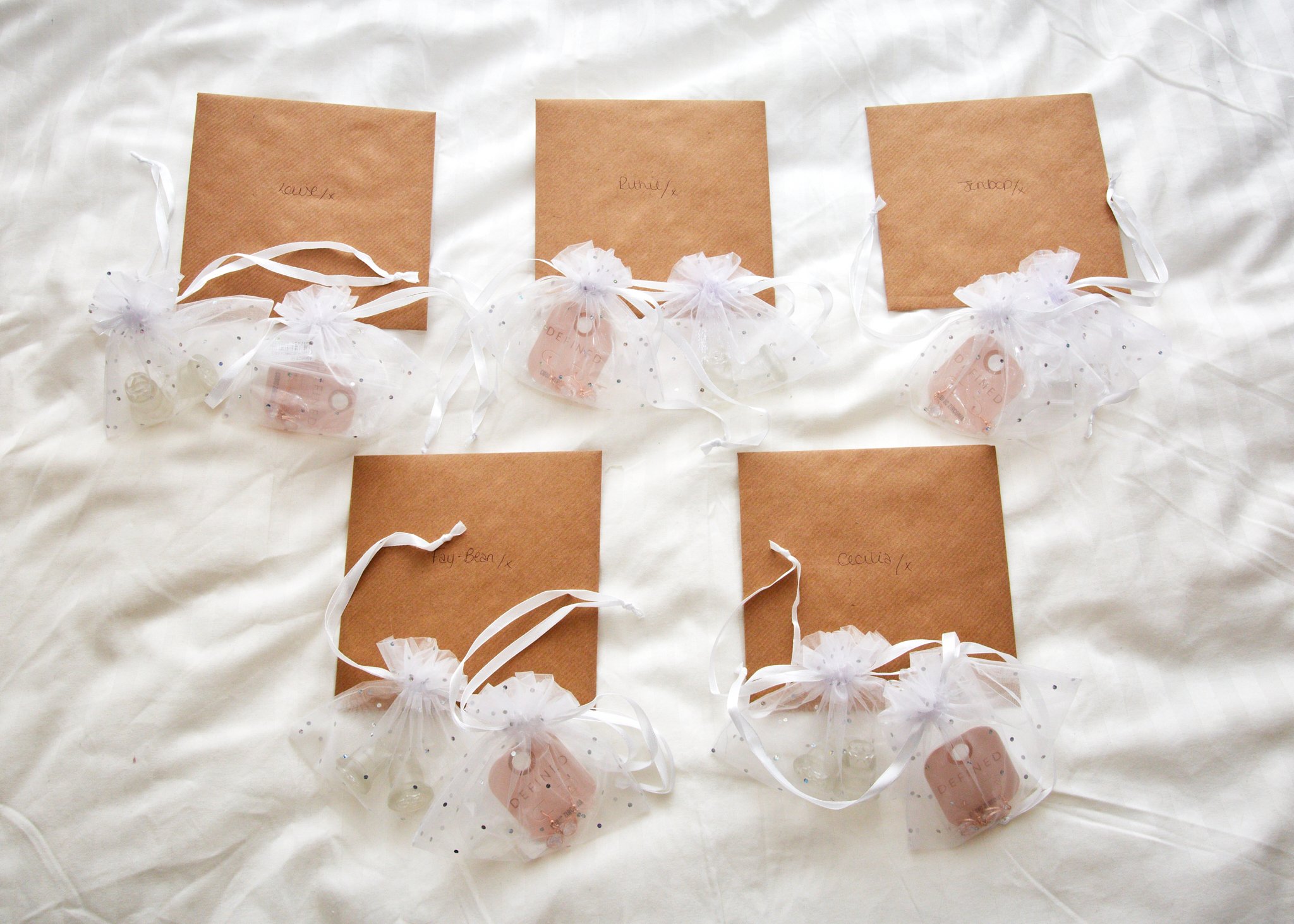 Several small gift bags with white ribbons and tissue paper, each labeled with a name, arranged on a white surface.