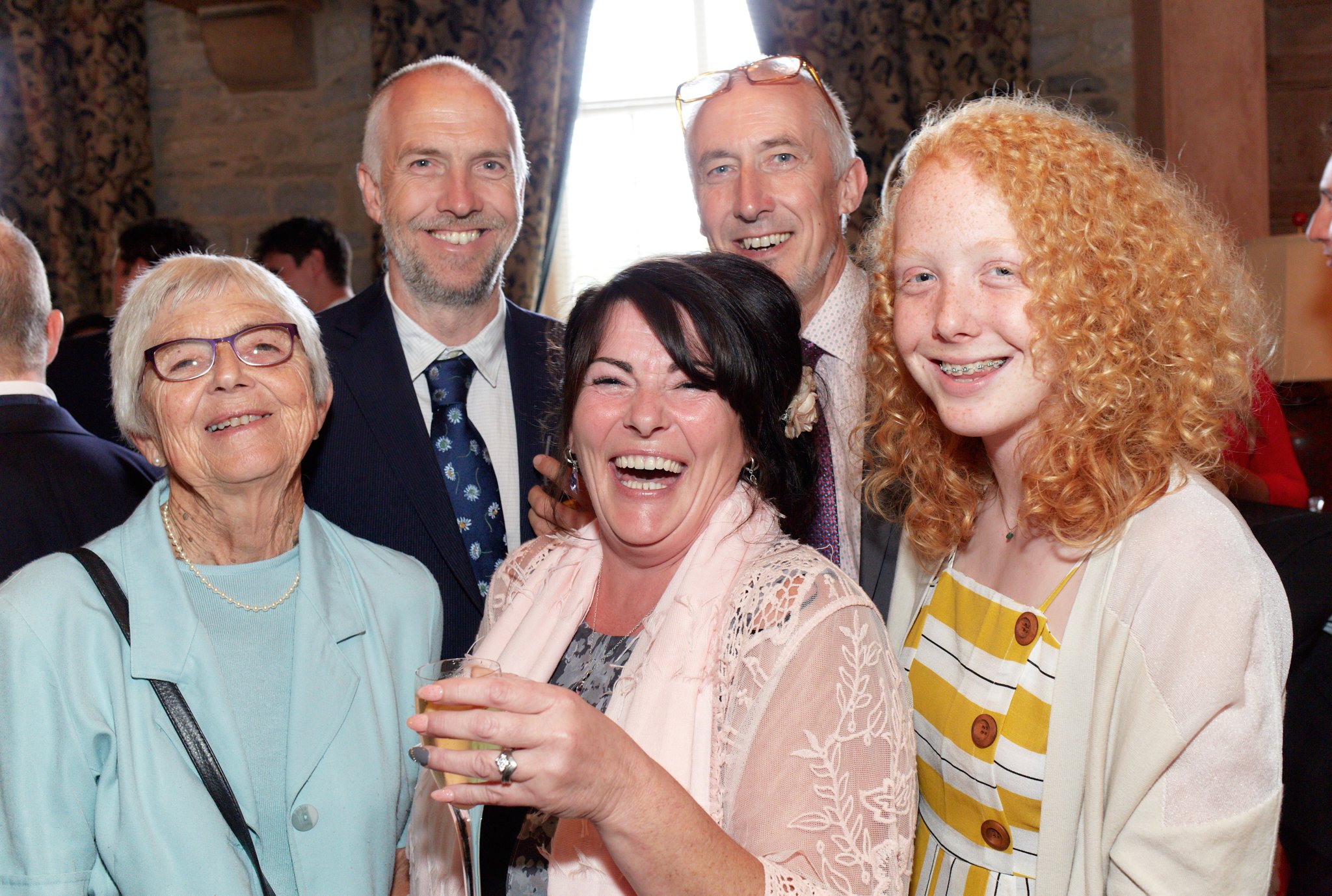 Group of six people at a social gathering smiling and enjoying drinks indoors.