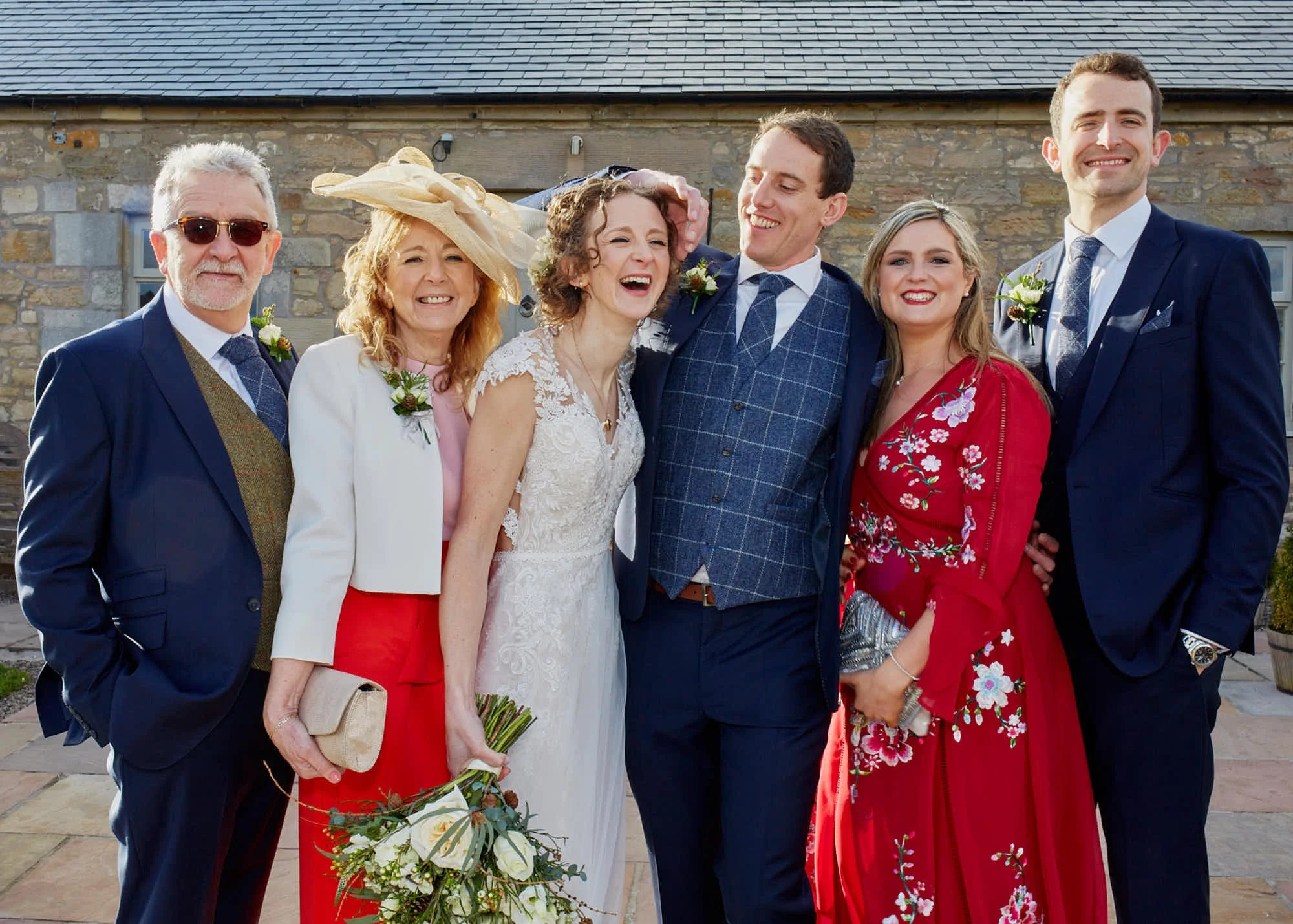 Group of seven people in formal attire at an outdoor event, smiling and standing close together.