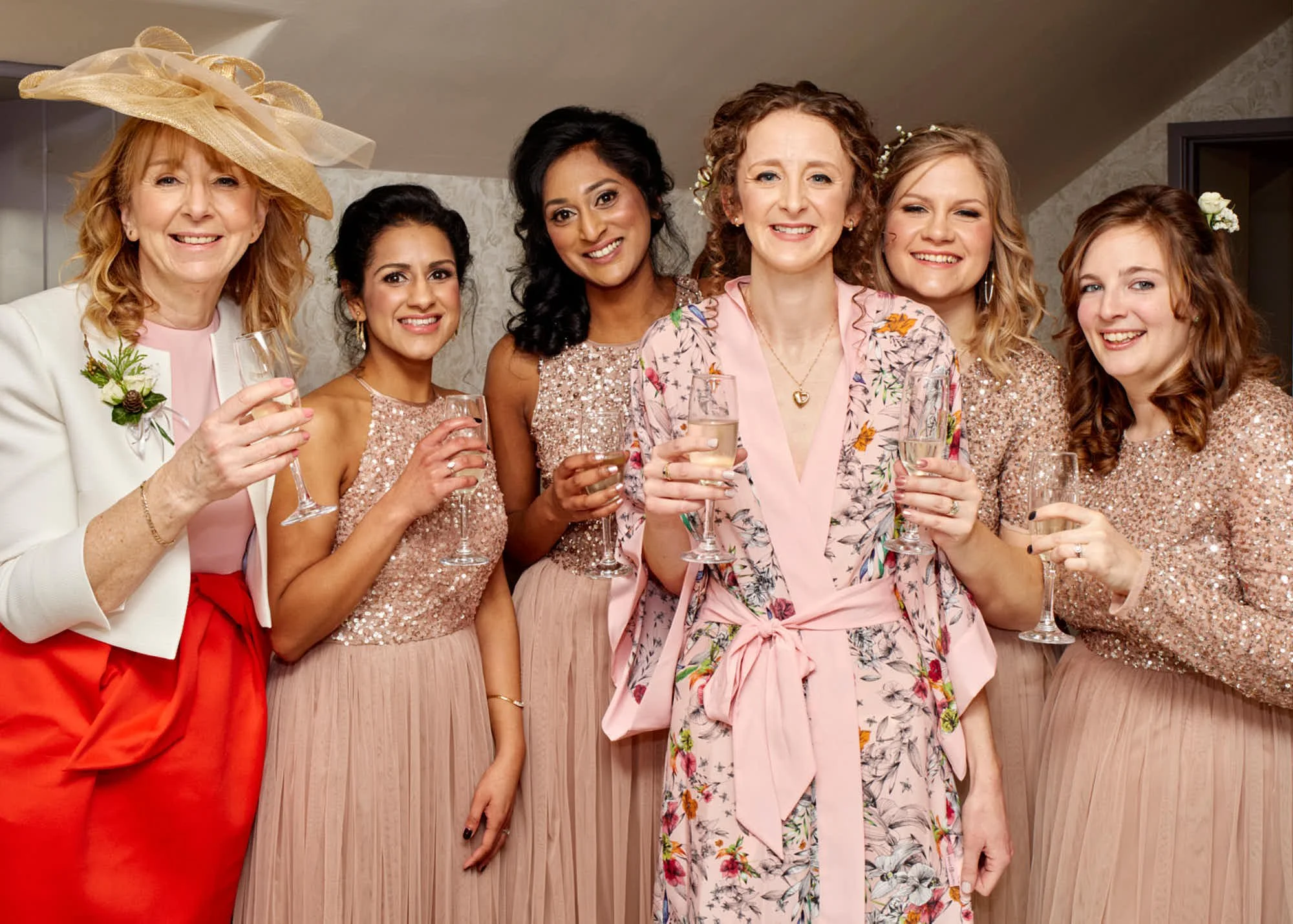 Group of women dressed in formal attire celebrating with champagne glasses, enjoying a festive gathering indoors.