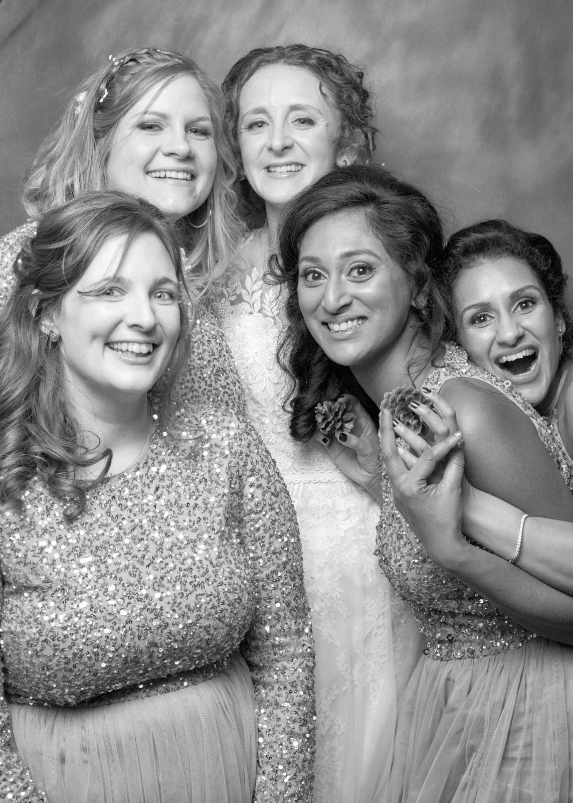 A group of six women dressed in formal attire, smiling and posing together in front of a plain background.