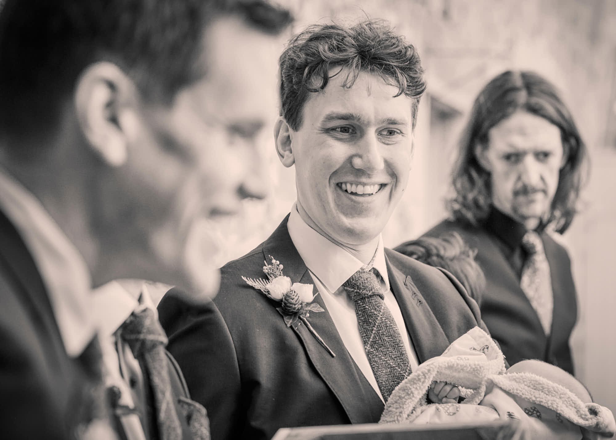 Black and white photo of men dressed in formal suits, sitting in a row, smiling and engaging in conversation.