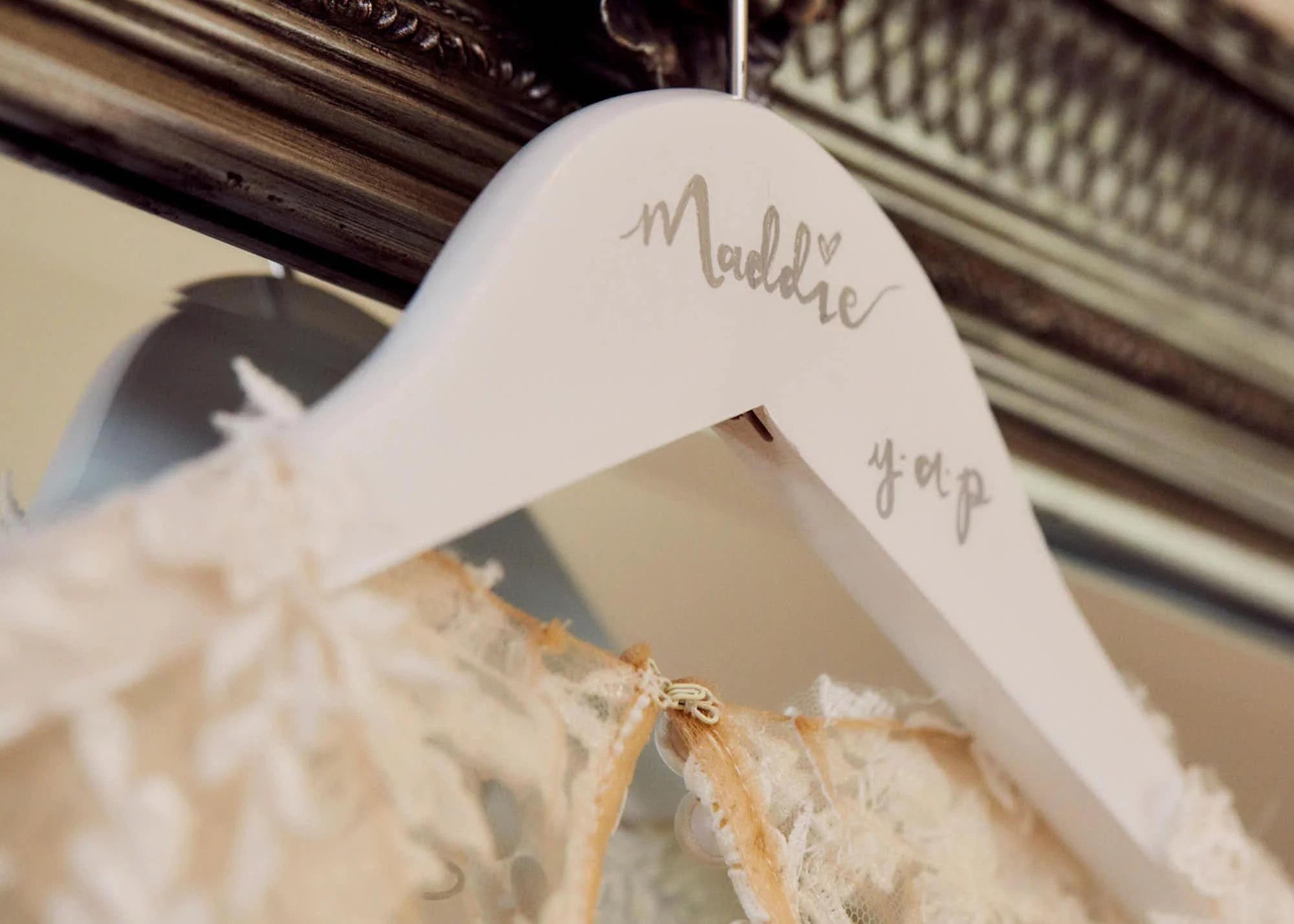 Close-up of a white decorative sign with the word 'Madeline' written in script and a small heart, hanging near a wooden furniture piece.