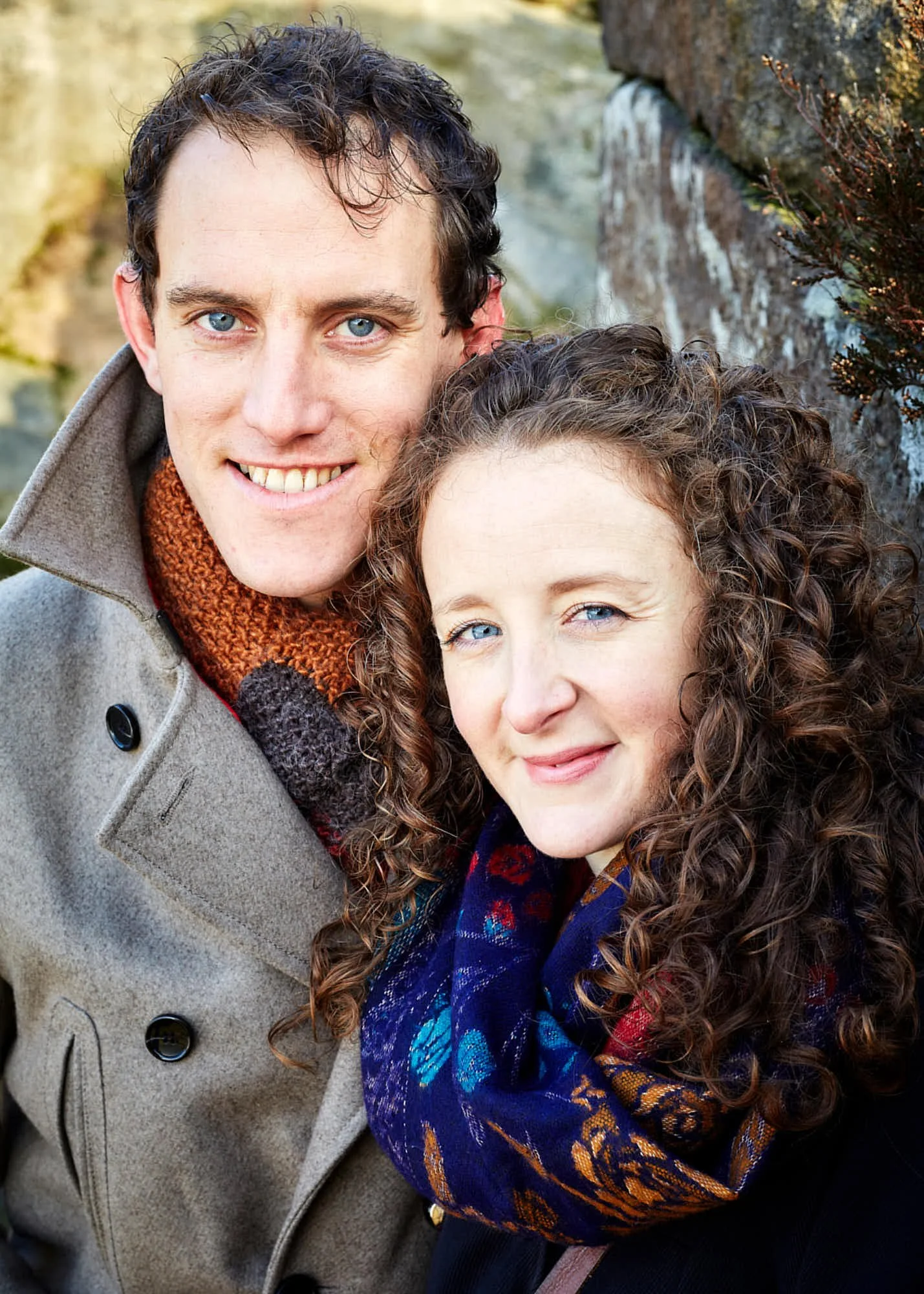 A man and woman smiling with their faces close together outdoors near a waterfall and rocks.