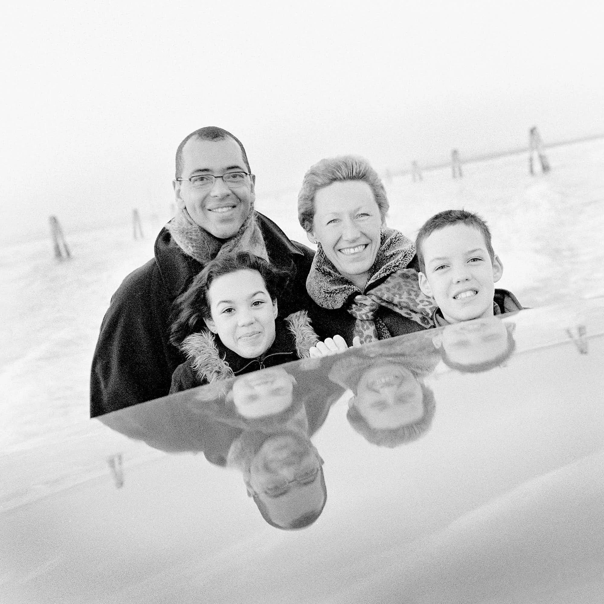 Black and white photo of a group of people smiling, standing closely together outdoors in winter, with snow on the ground in the background.