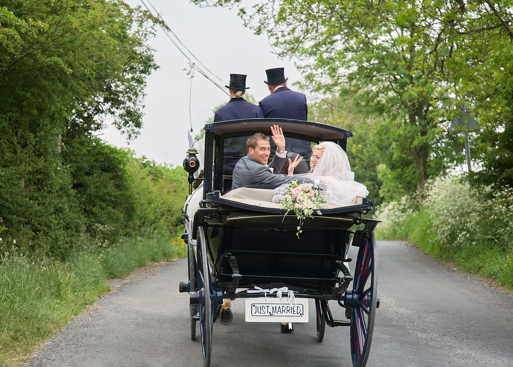 A newly married couple sitting in a horse-drawn carriage decorated with flowers, with a 