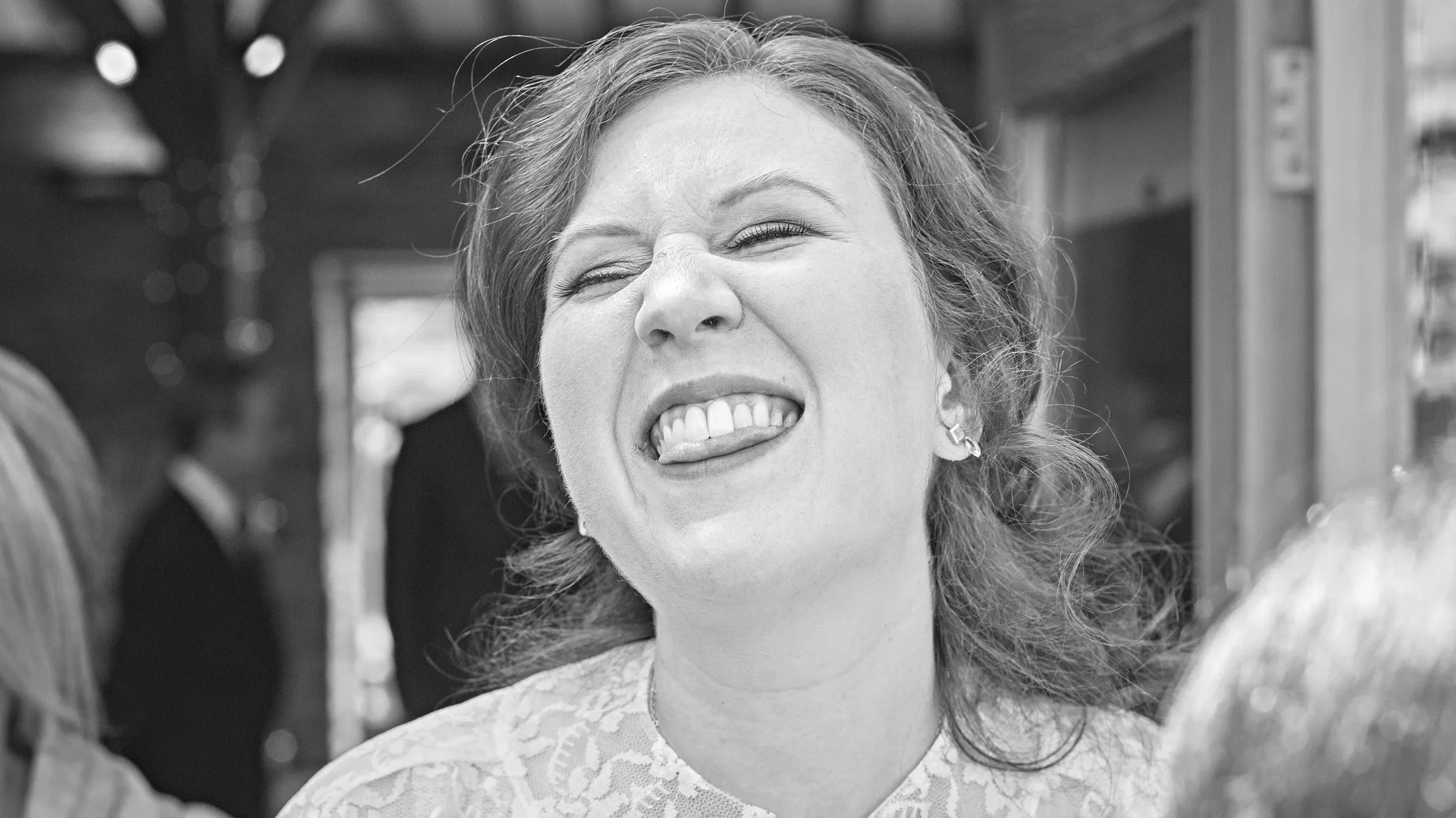 Close-up of a woman with curly hair and earrings making a silly face with her tongue out and eyes squinted, smiling.