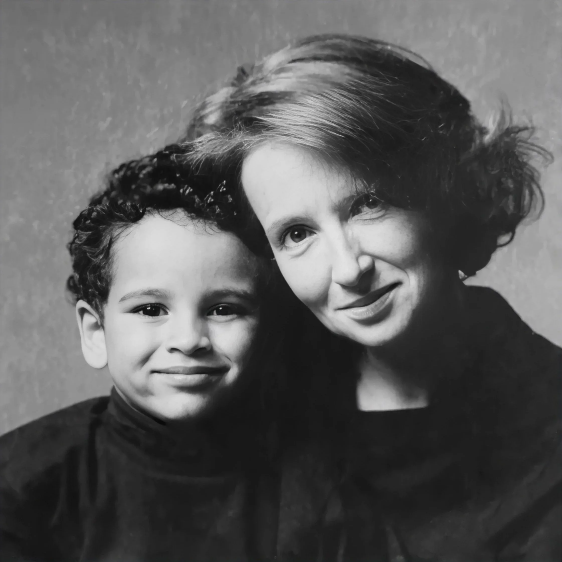 A black and white photograph of two women and a young girl, all smiling. The women have curly hair, and the girl has straight hair and is wearing a collared shirt.