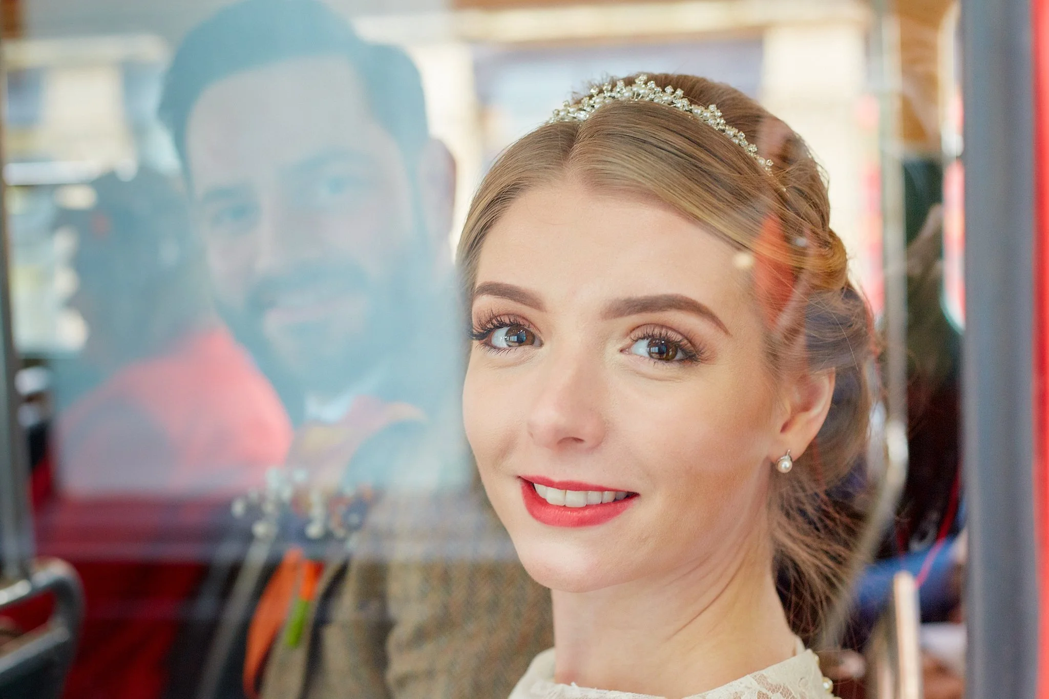 A woman with styled brown hair, wearing pearl earrings and a pearl headband, smiling behind a glass display case with colorful objects.