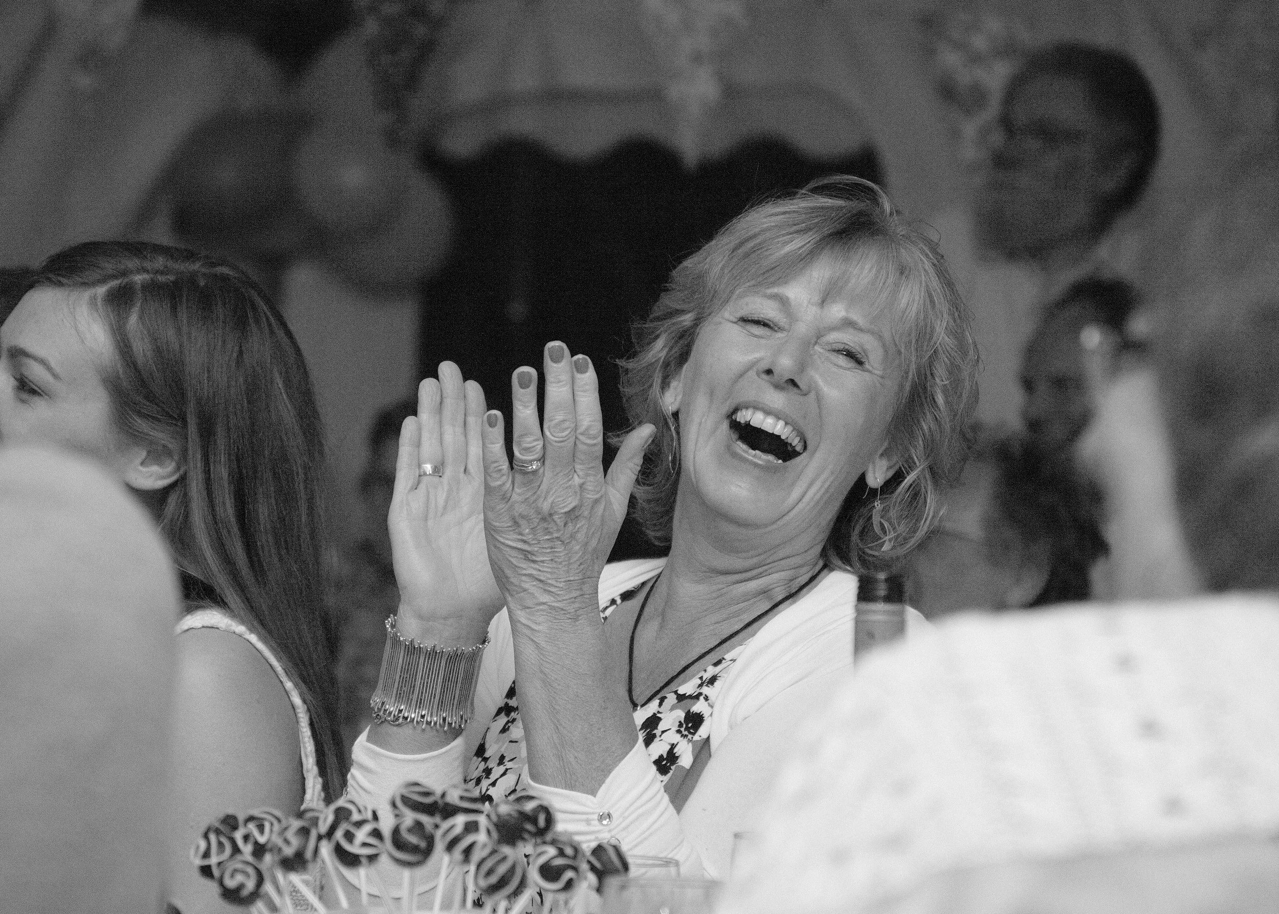 A black and white photo of a woman laughing and waving her hand, with several children and other people around her in a social setting.