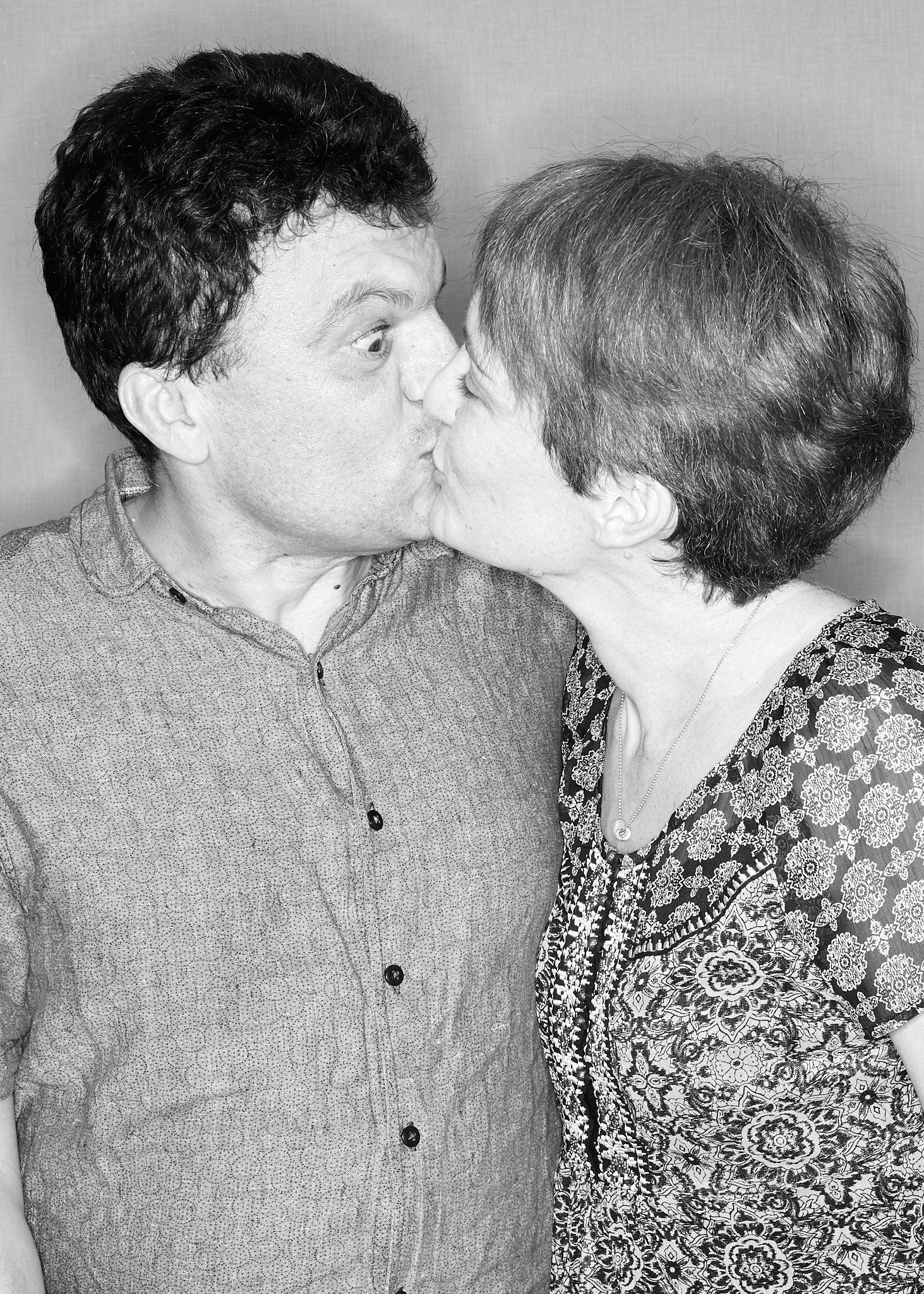 A black and white photo of a man and woman kissing face-to-face with noses touching, smiling, and eyes closed.
