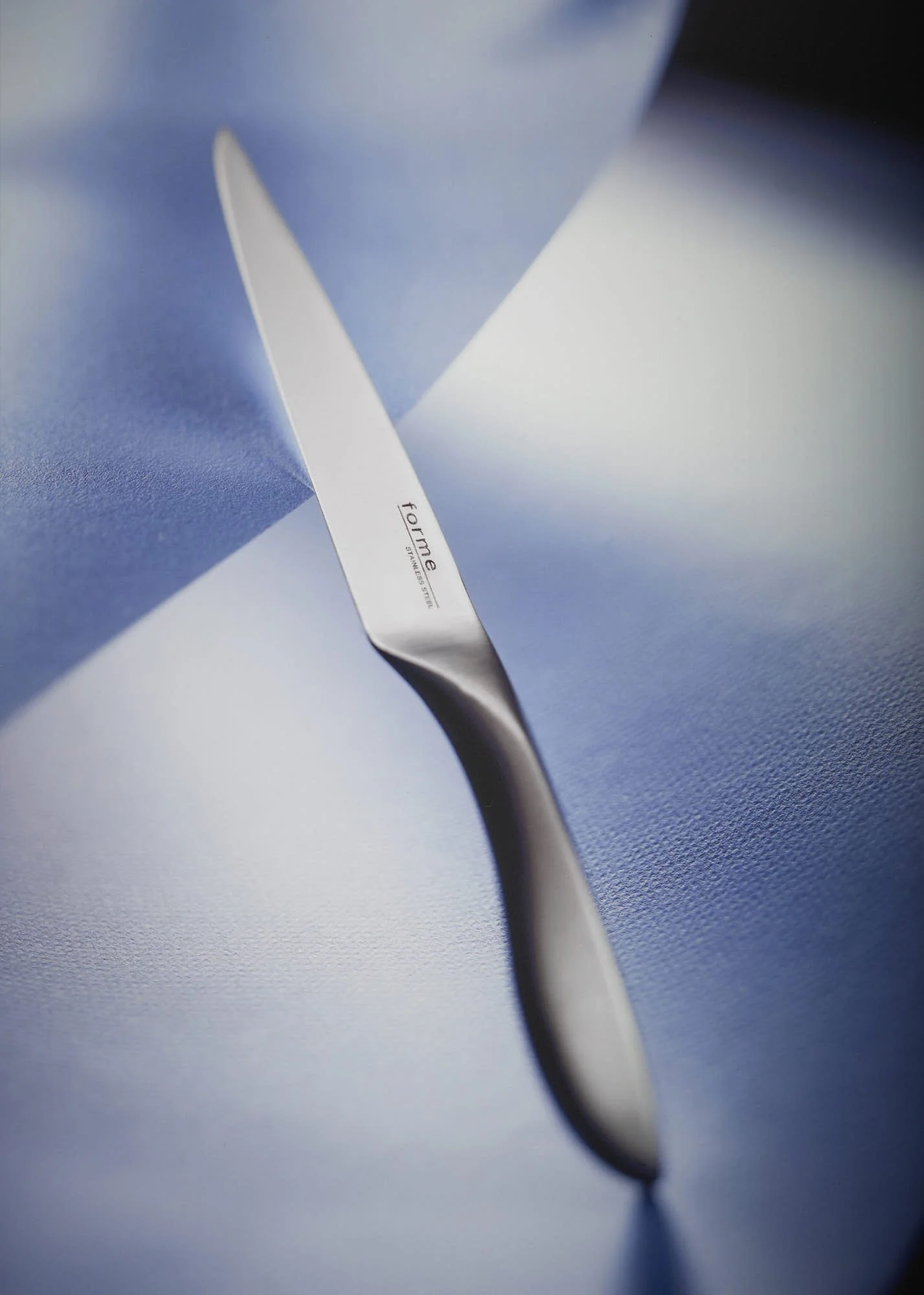 Close-up of a stainless steel knife resting on blue paper, with part of its handle visible.