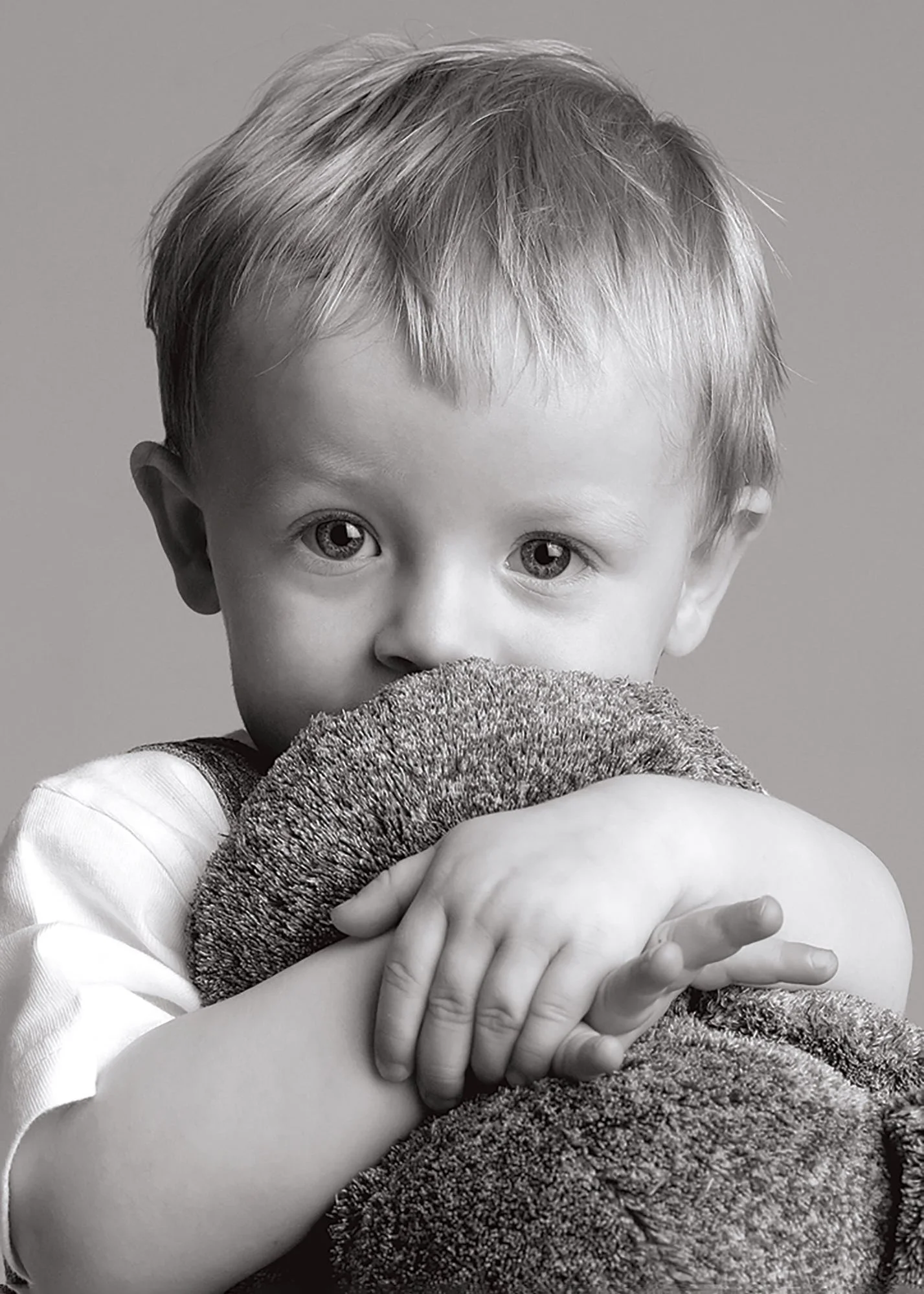 A young boy hugging a blanket, looking at the camera with big eyes, black and white photograph.