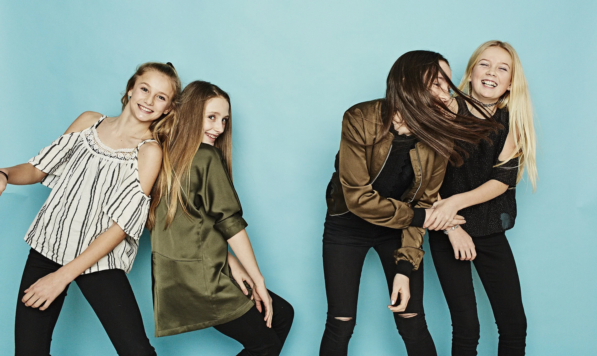 Five young women standing together against a blue background, smiling and posing playfully.