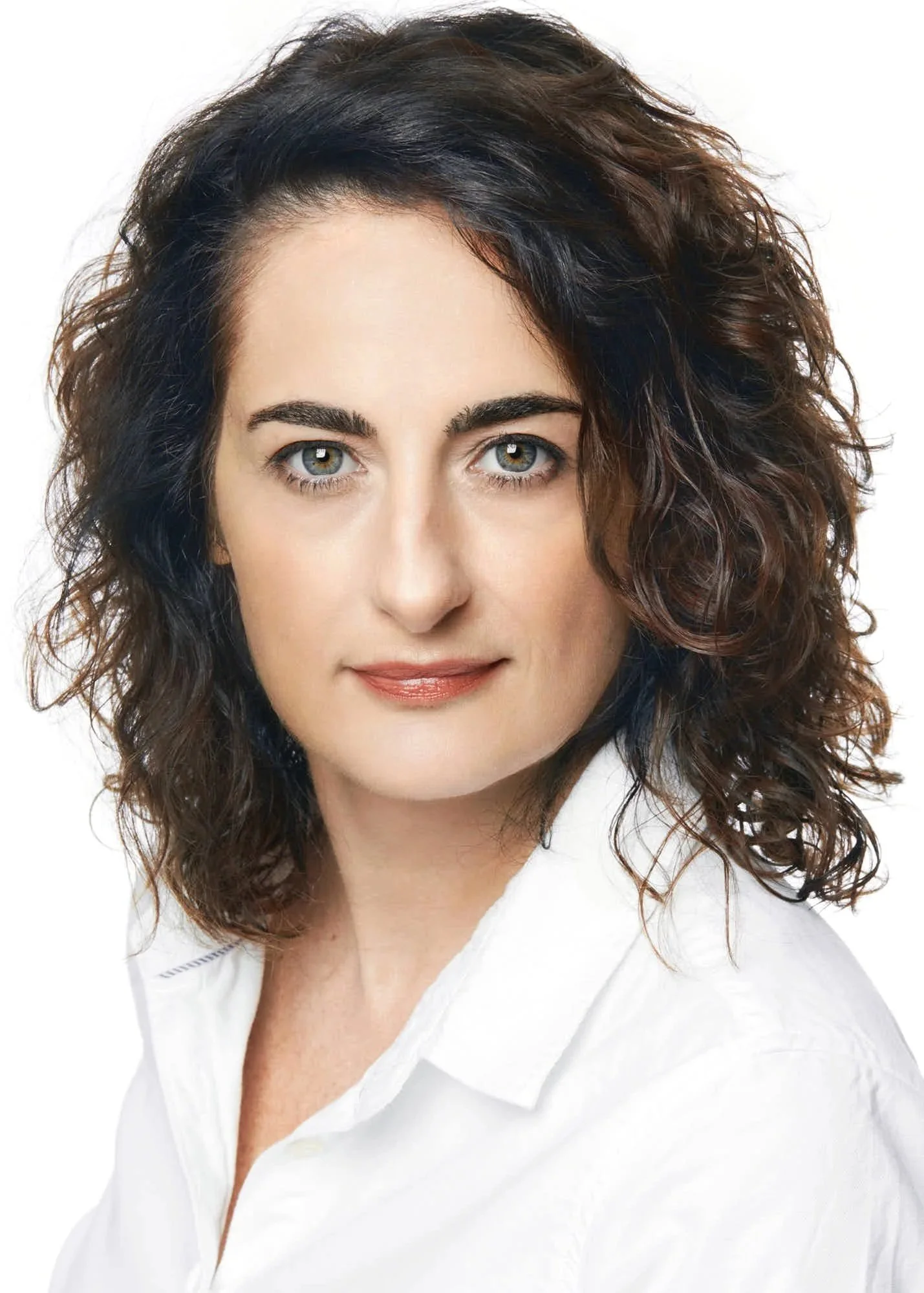 A woman with curly brown hair and striking blue eyes wearing a white shirt.