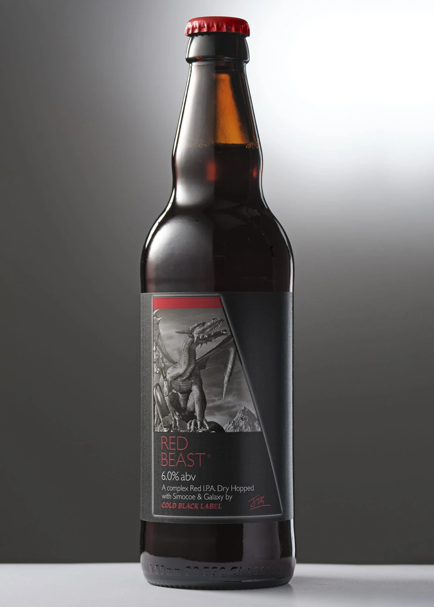 A dark beer bottle with a red cap, featuring a grayscale illustration of a dragon on the label and the words 'Red Beast' and 'Cold Black Label' in red.