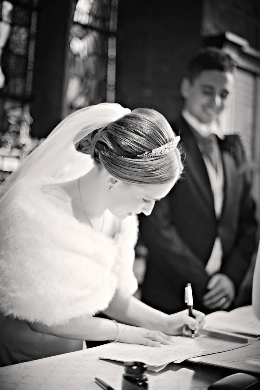 Bride signing marriage documents with groom and officiant present, in a wedding ceremony.