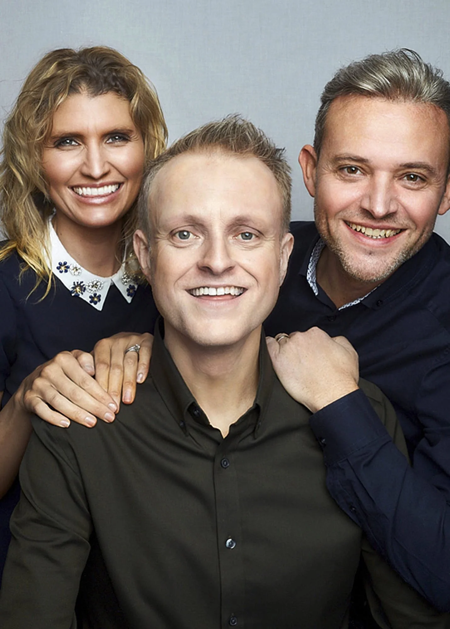 Four people smiling close together, with two men and two women, in a friendly group portrait.