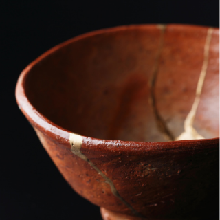 Close-up of a reddish-brown ceramic bowl with a crackle glaze against a black background.