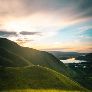 Scenic view of green rolling hills at sunset with a cloudy sky and a distant river.