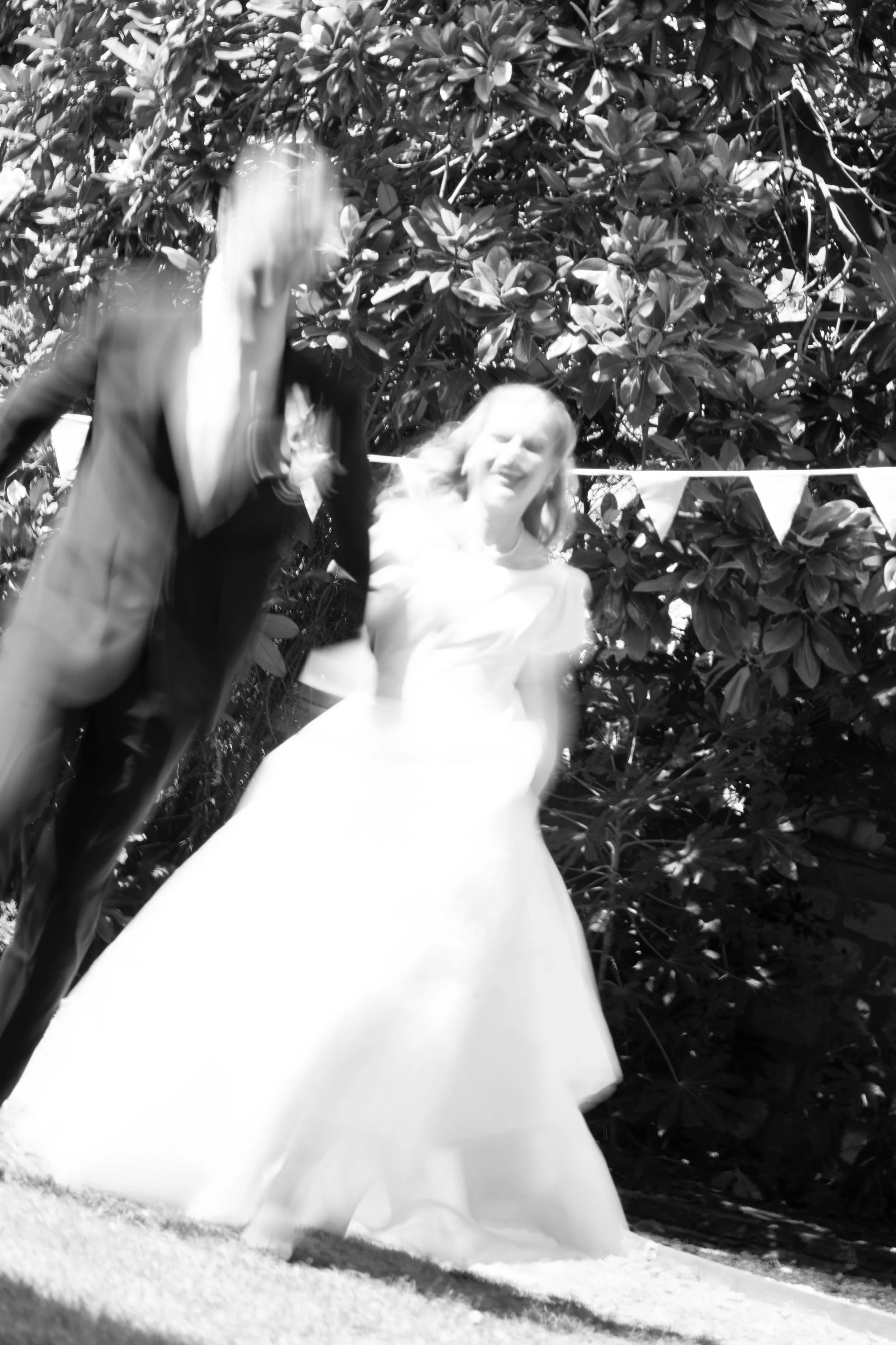 A bride in a wedding dress standing outdoors with greenery in the background.
